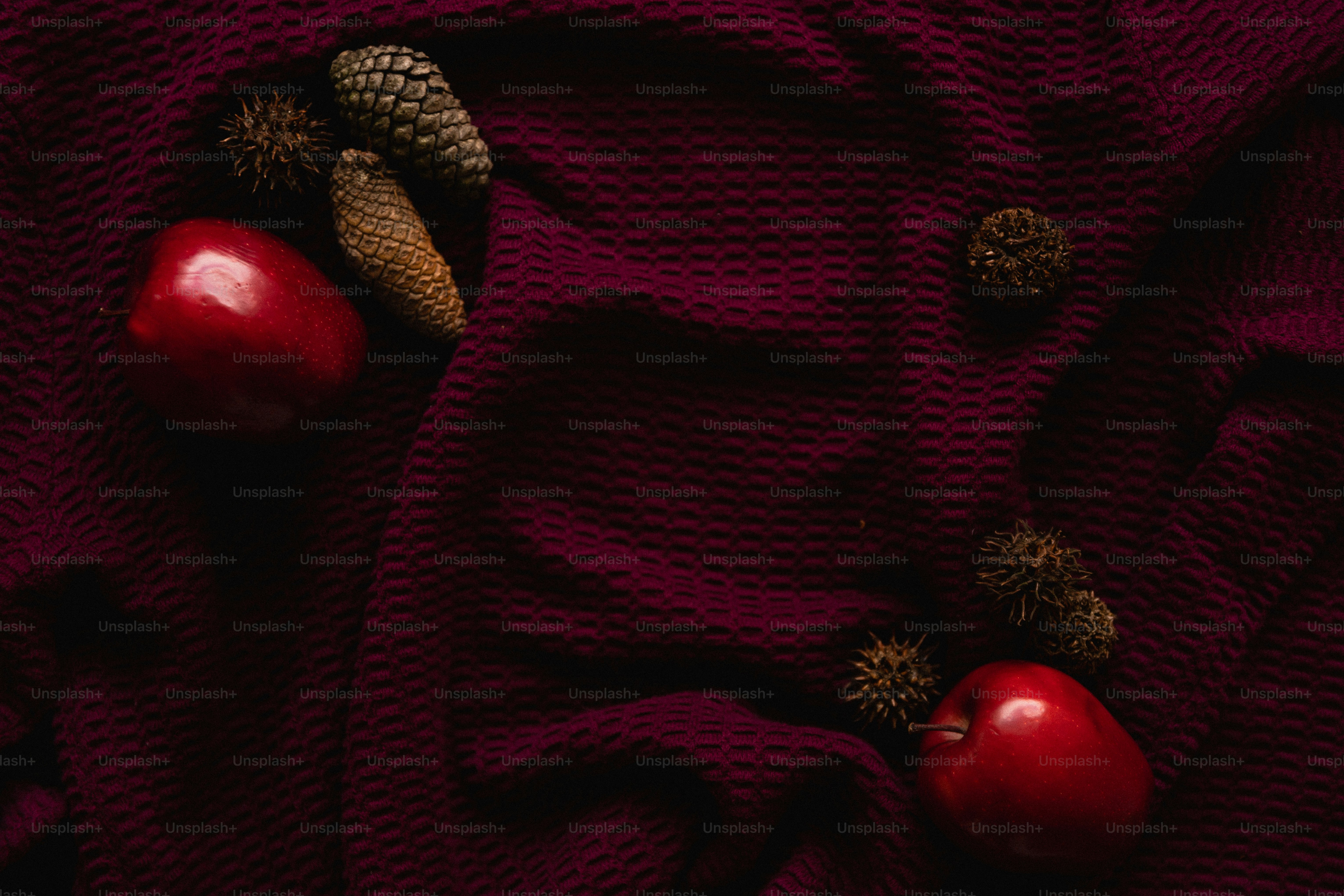 Two red apples and pinecones on a burgundy cloth