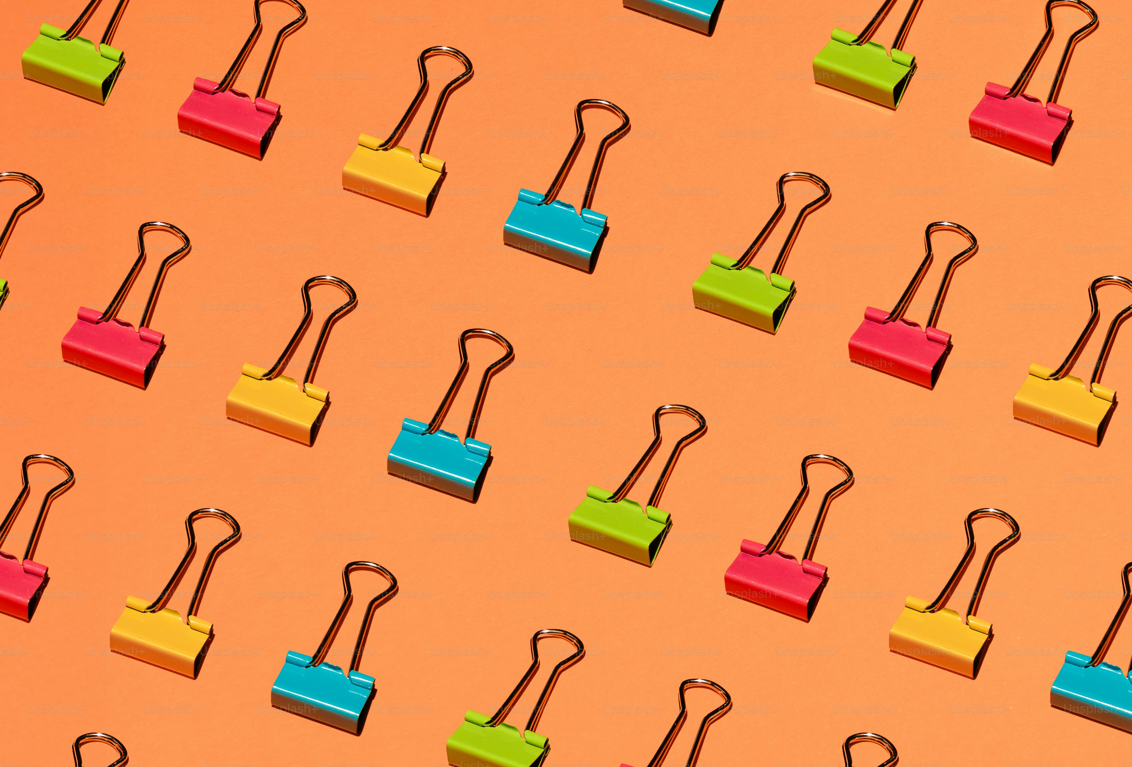 Colorful binder clips arranged in a pattern on orange background