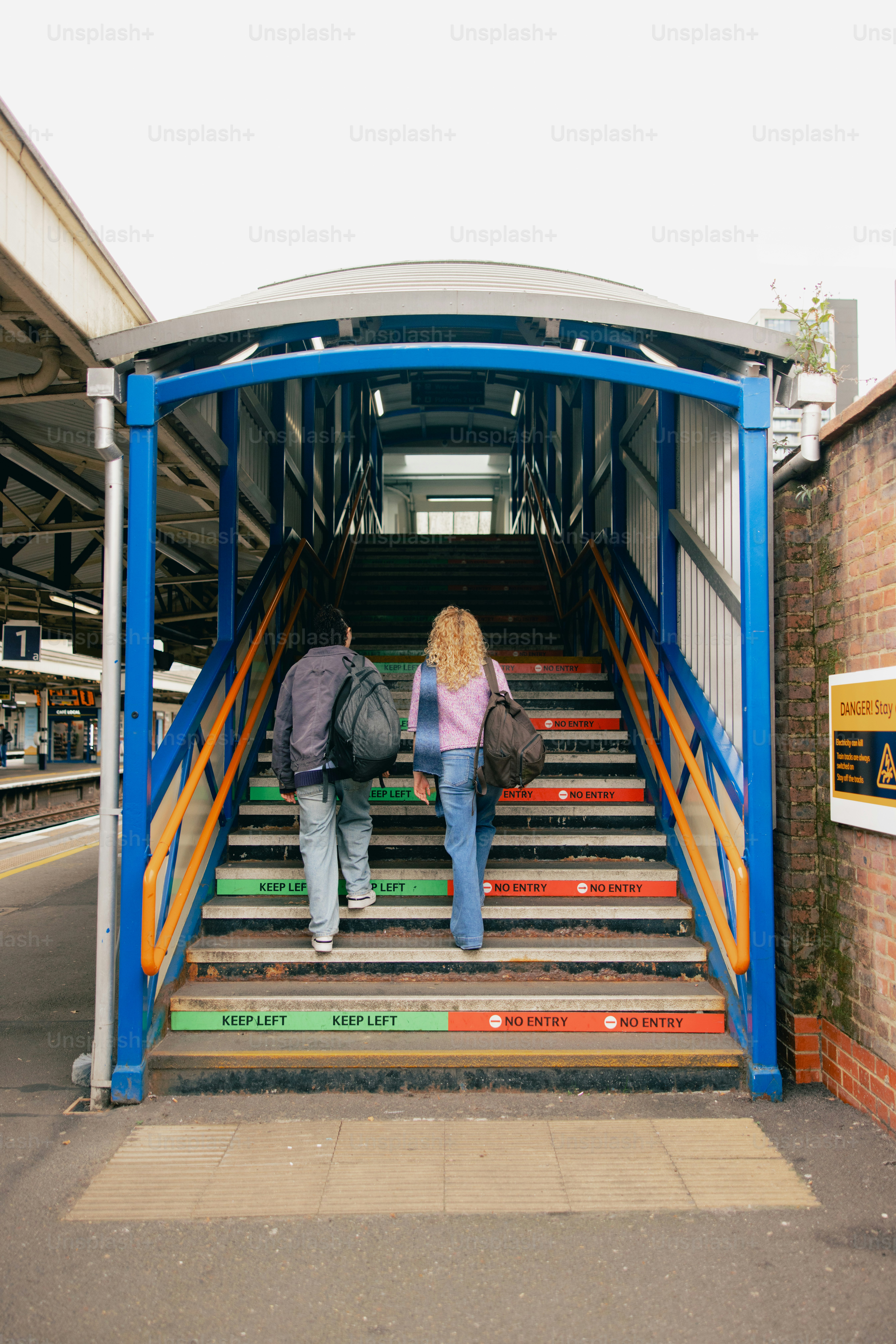 Two people ascend colorful stairs at a train station.