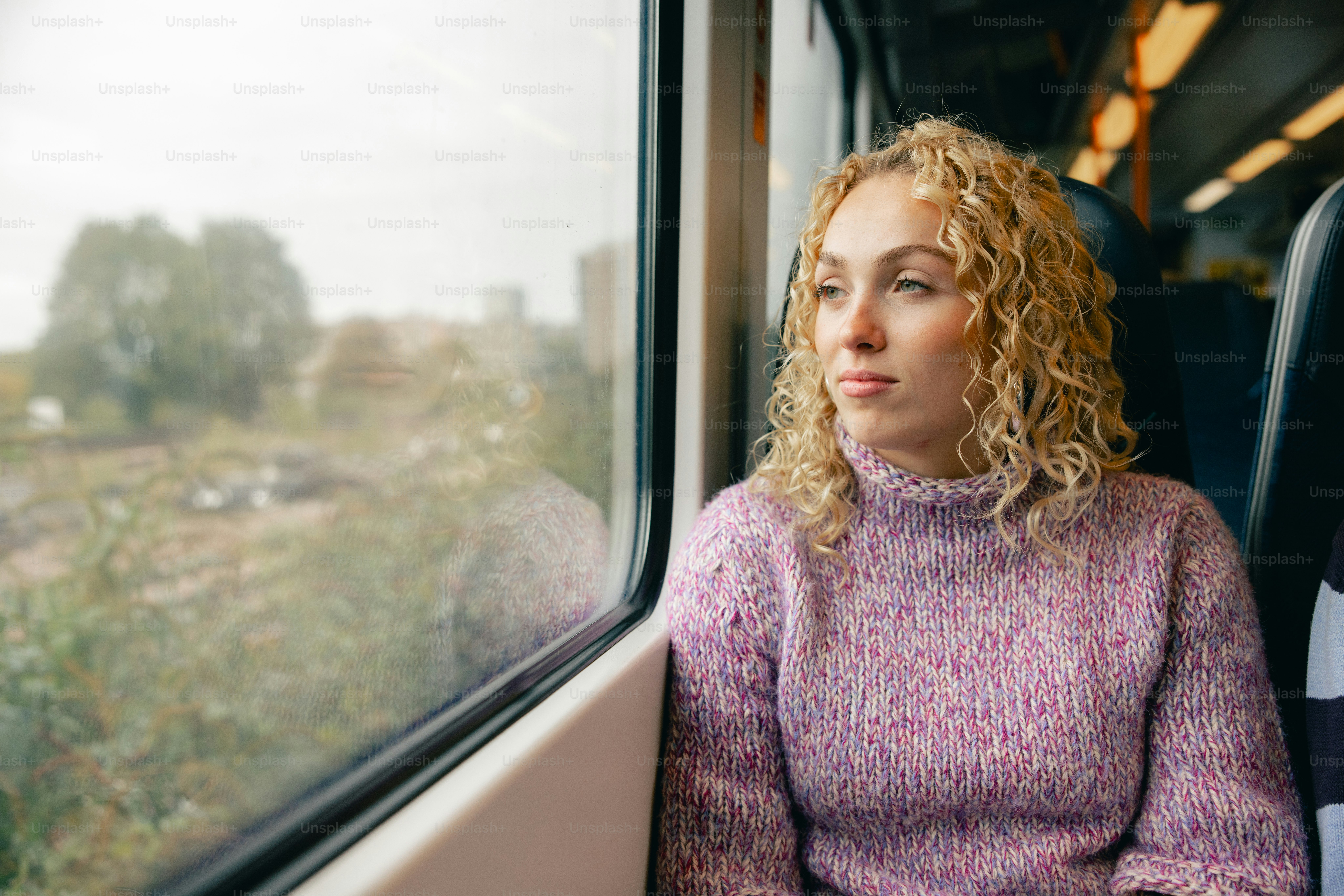 Mujer joven con cabello rizado mirando por la ventana del tren