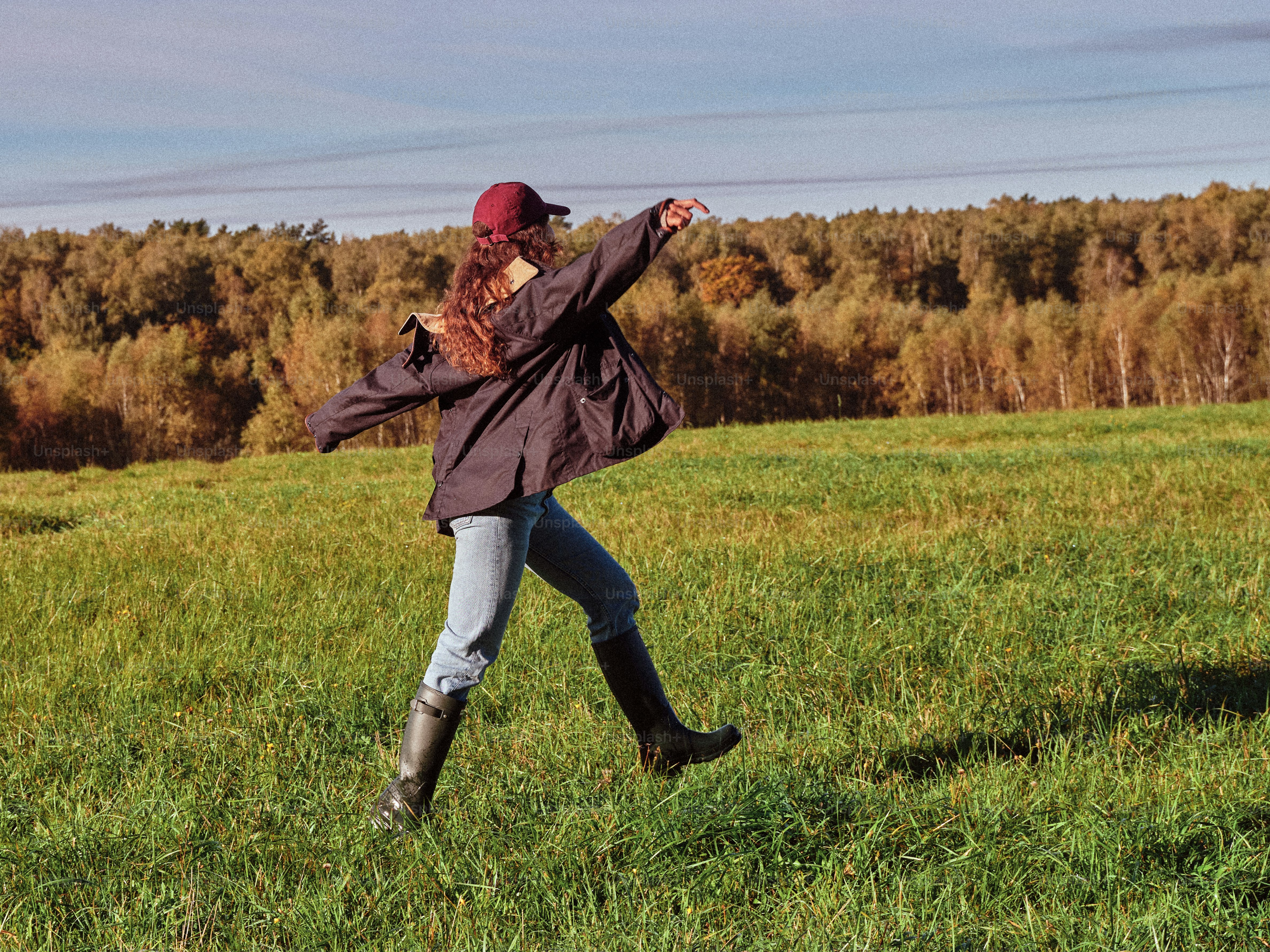 ジーンズとブーツを履いた女性が芝生の野原を走っている。