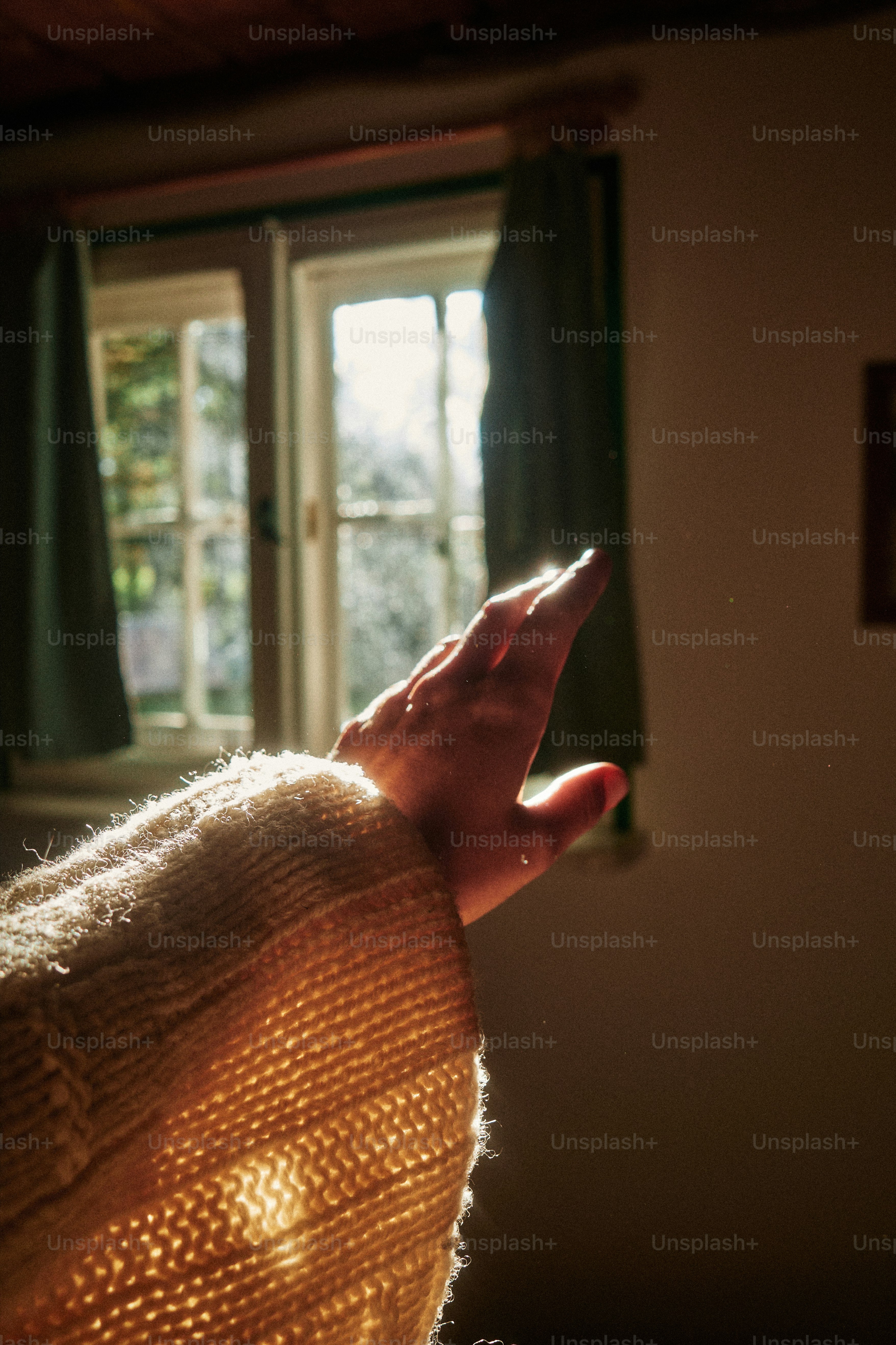 Hand reaching towards sunlight streaming through window.