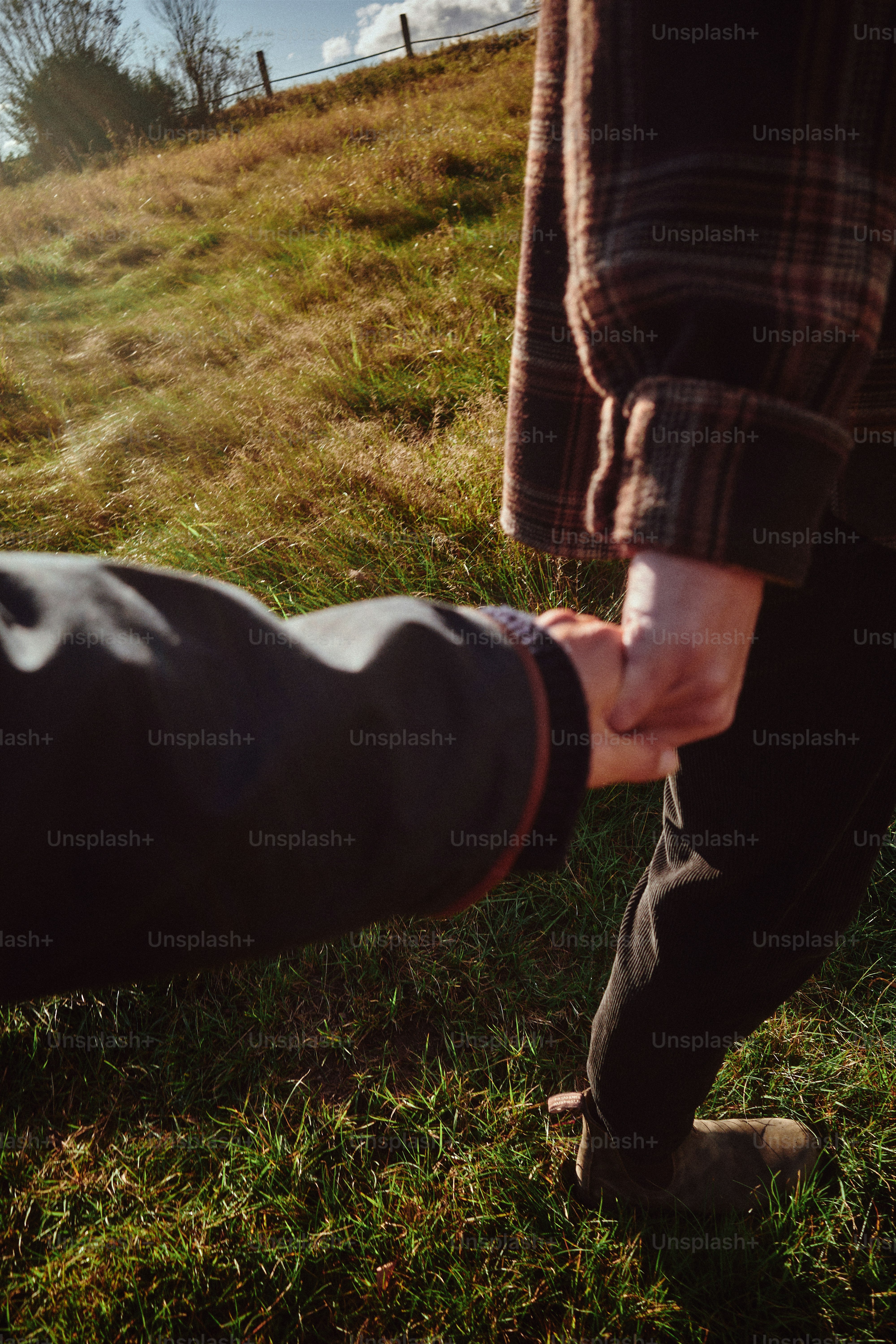 手をつないで草の丘を歩く二人。