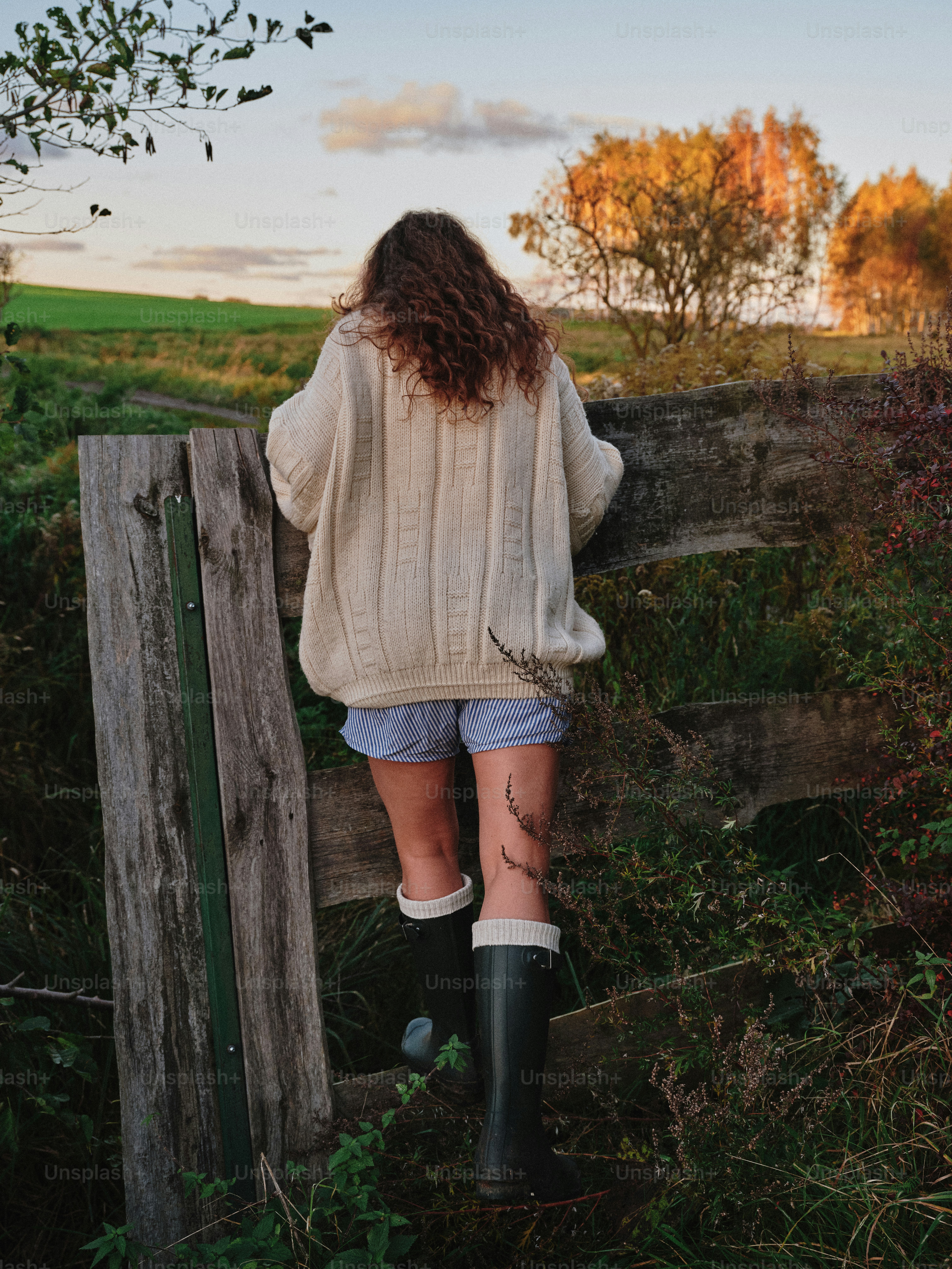 Woman climbing over wooden fence at sunset