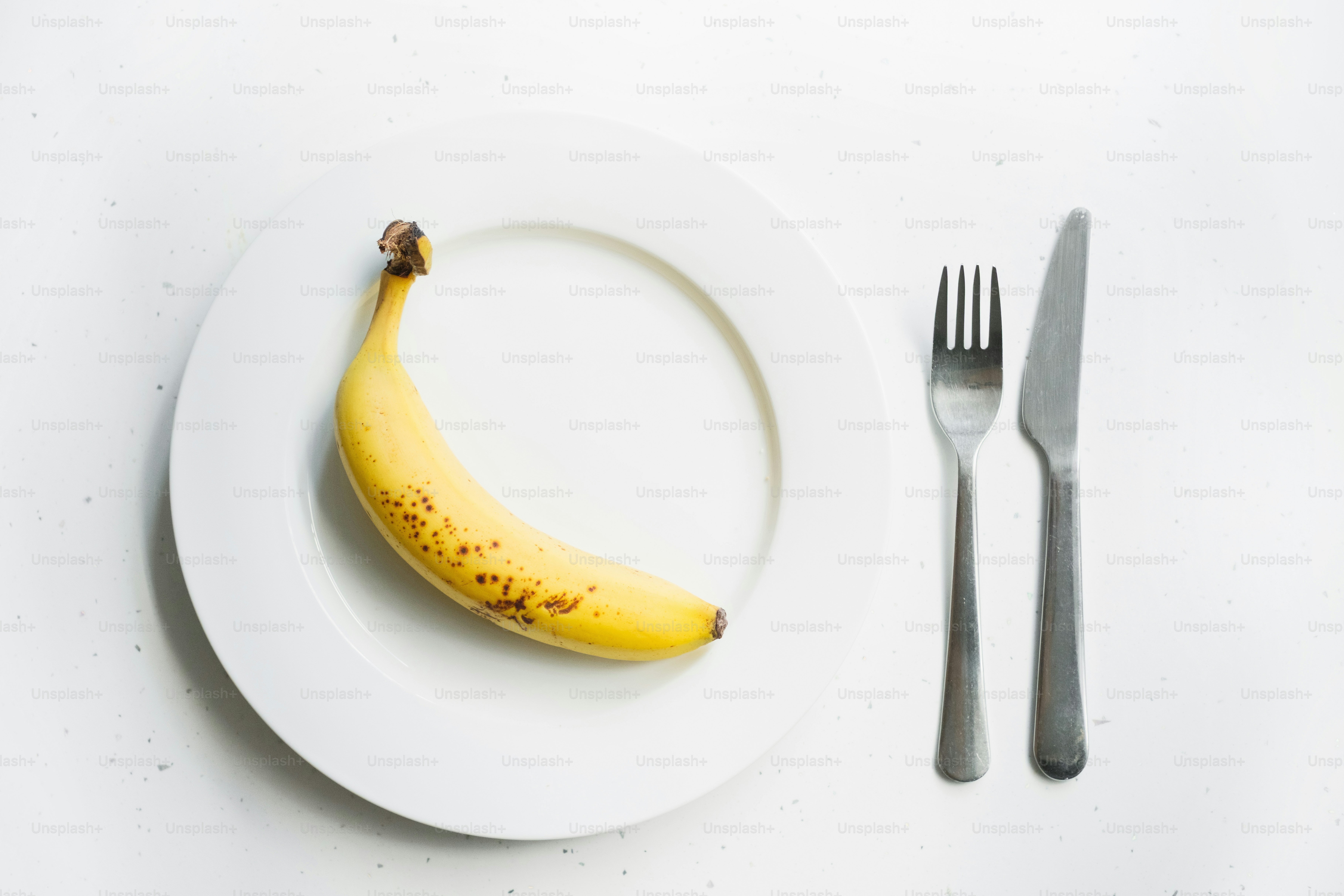 A single banana on a white plate with cutlery.