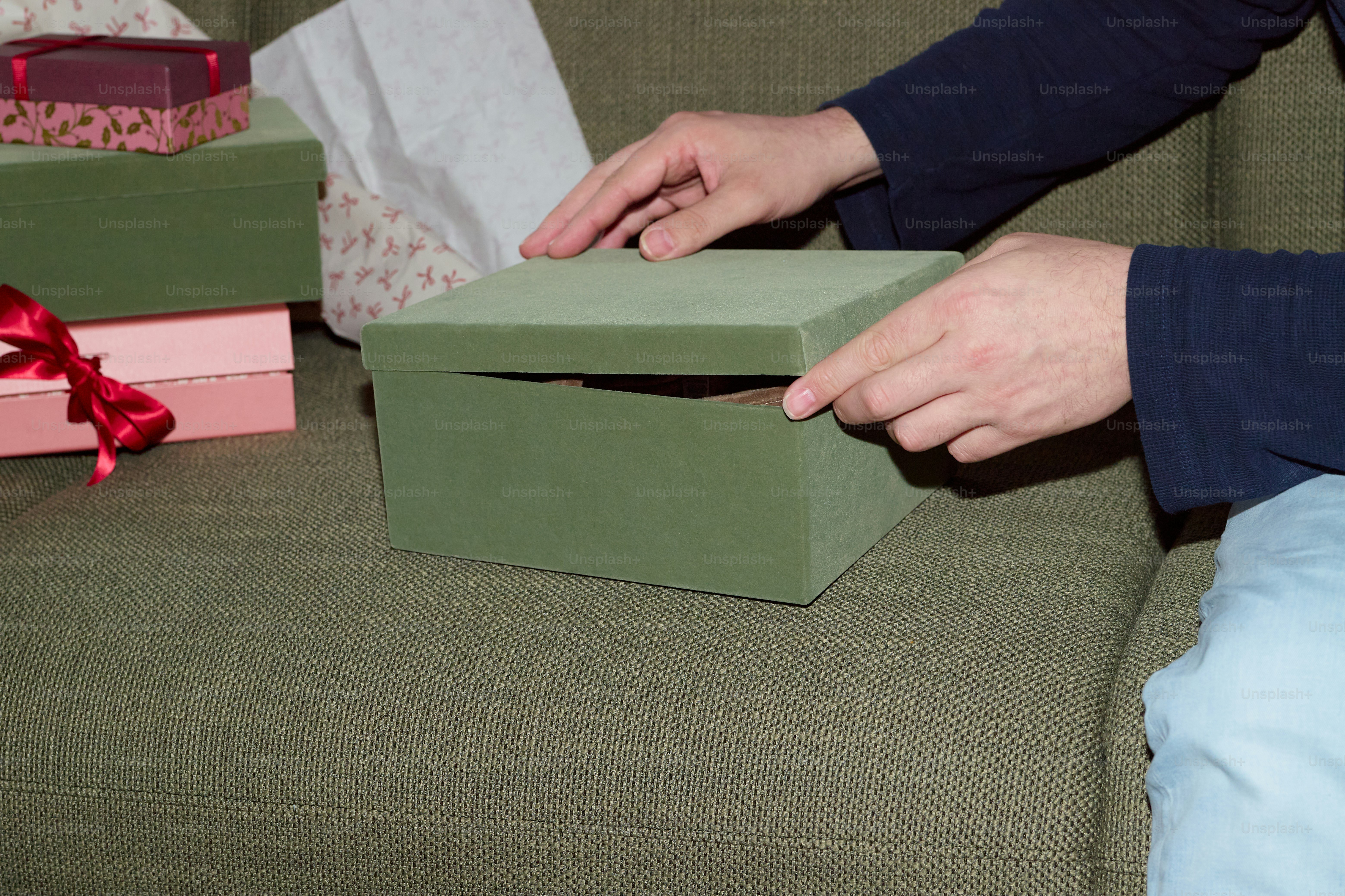 Hands opening a green gift box on a couch