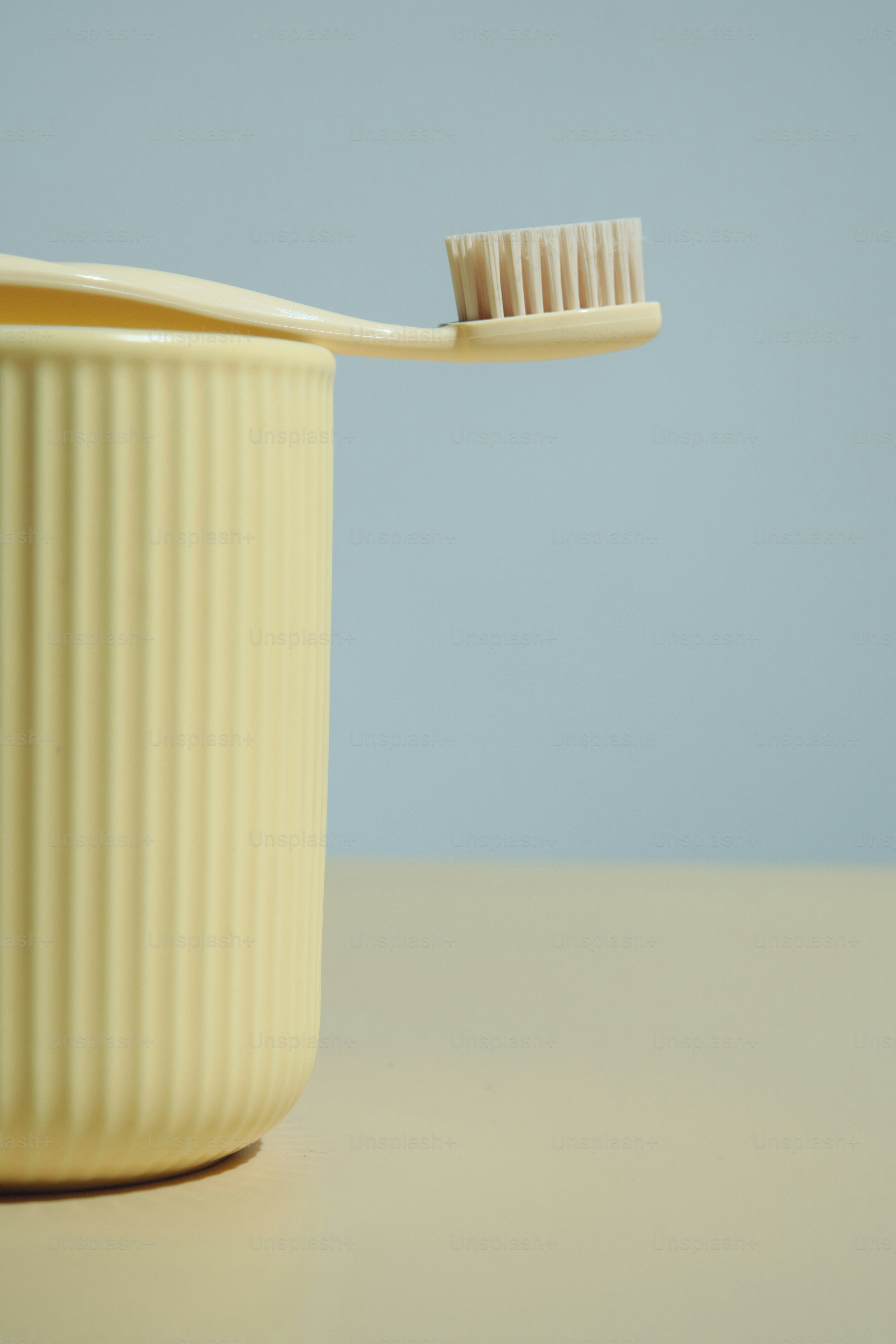 A yellow toothbrush rests on a ribbed cup.