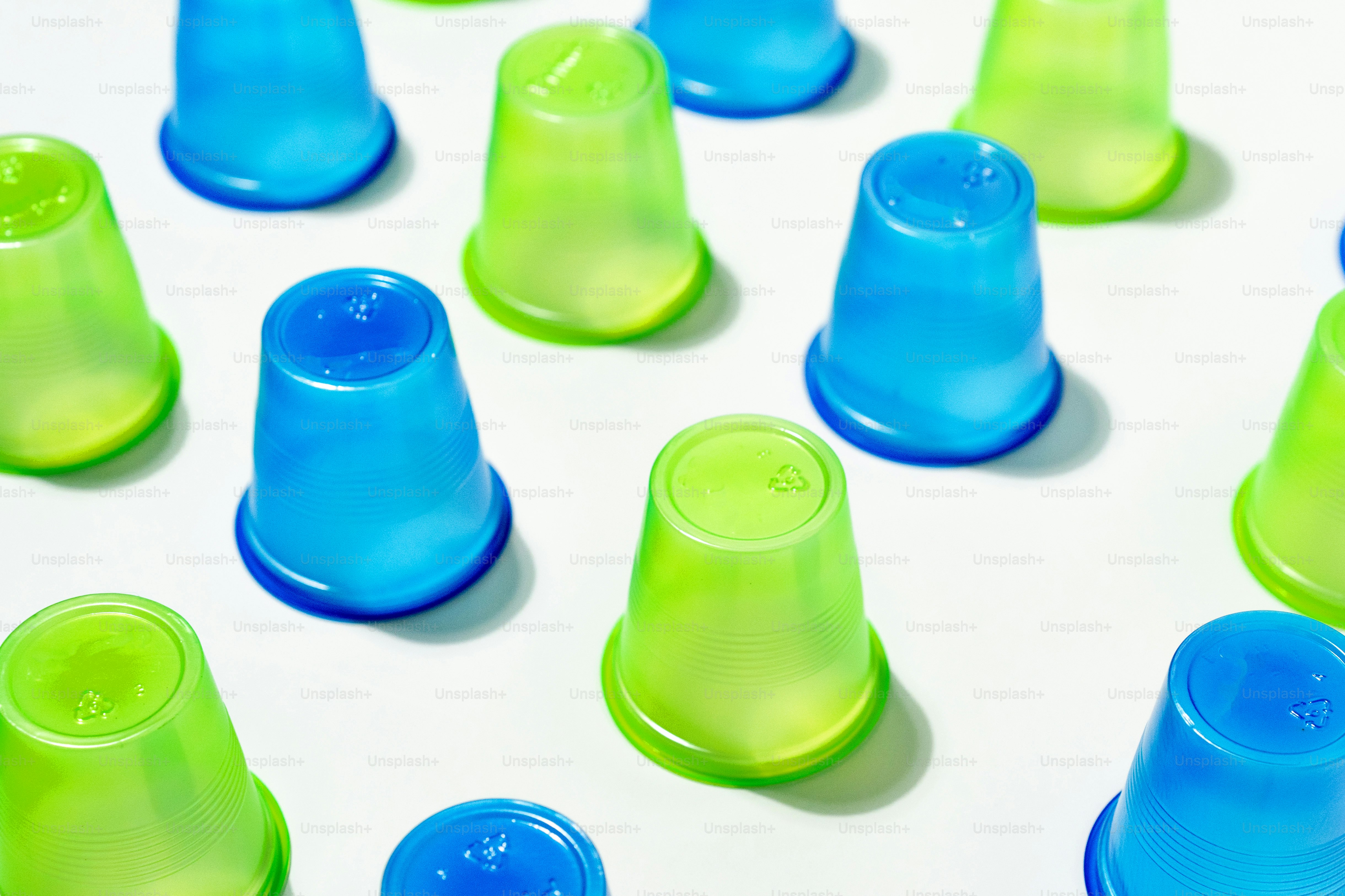 Filas de vasos de plástico azul y verde sobre fondo blanco