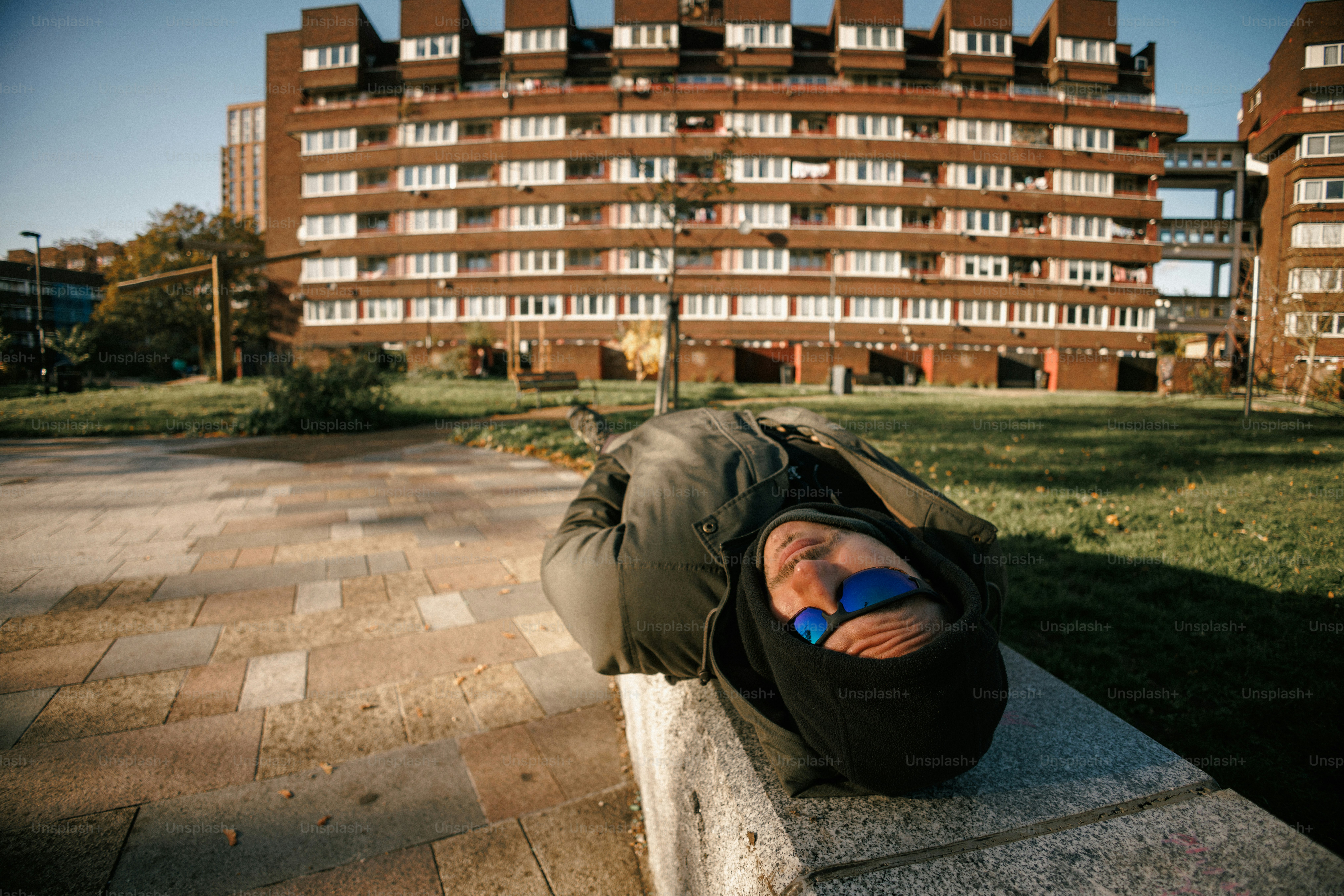 Homeless person sleeping on a concrete ledge outdoors.