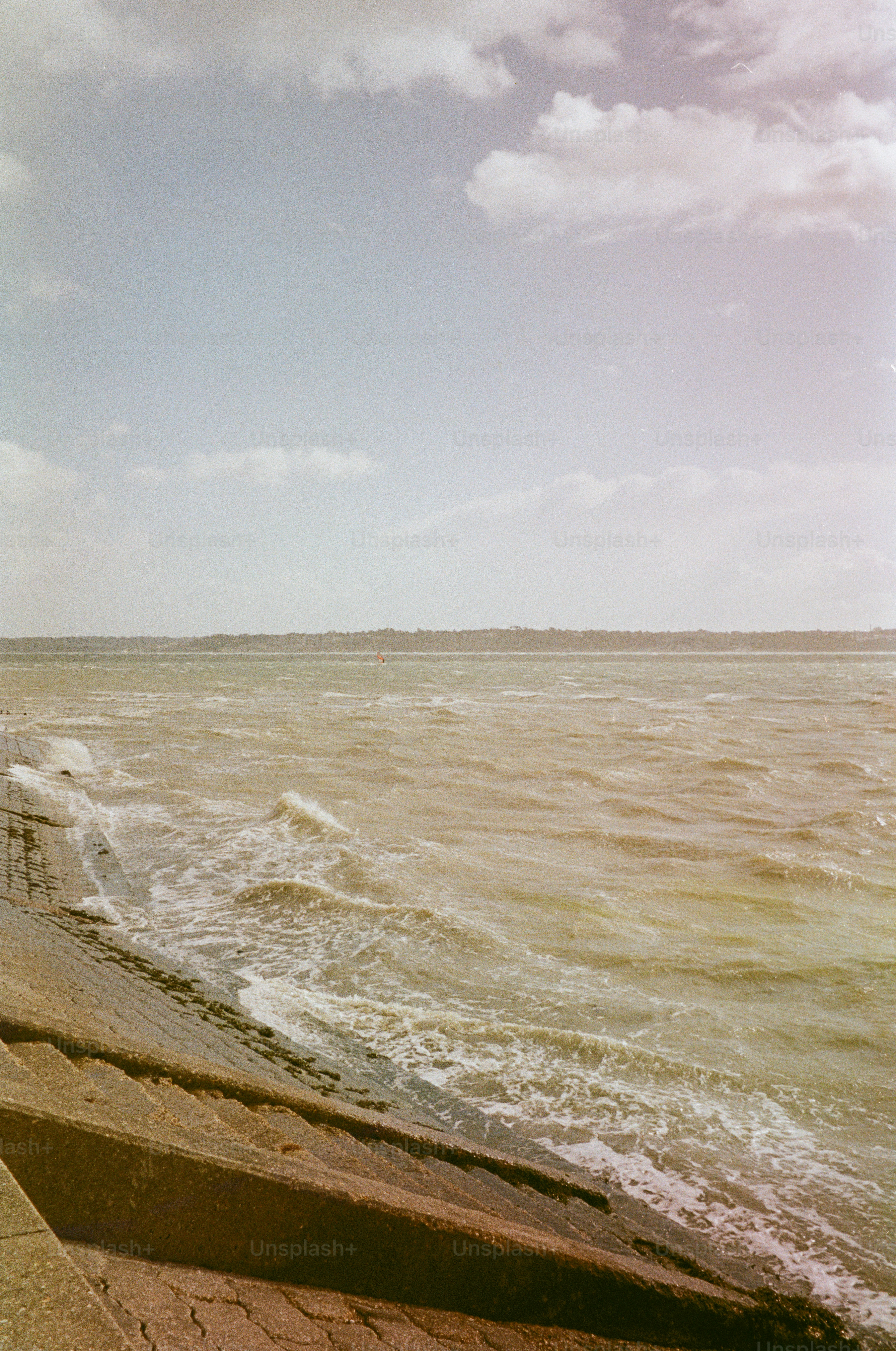 Waves crash against a concrete embankment under a cloudy sky.