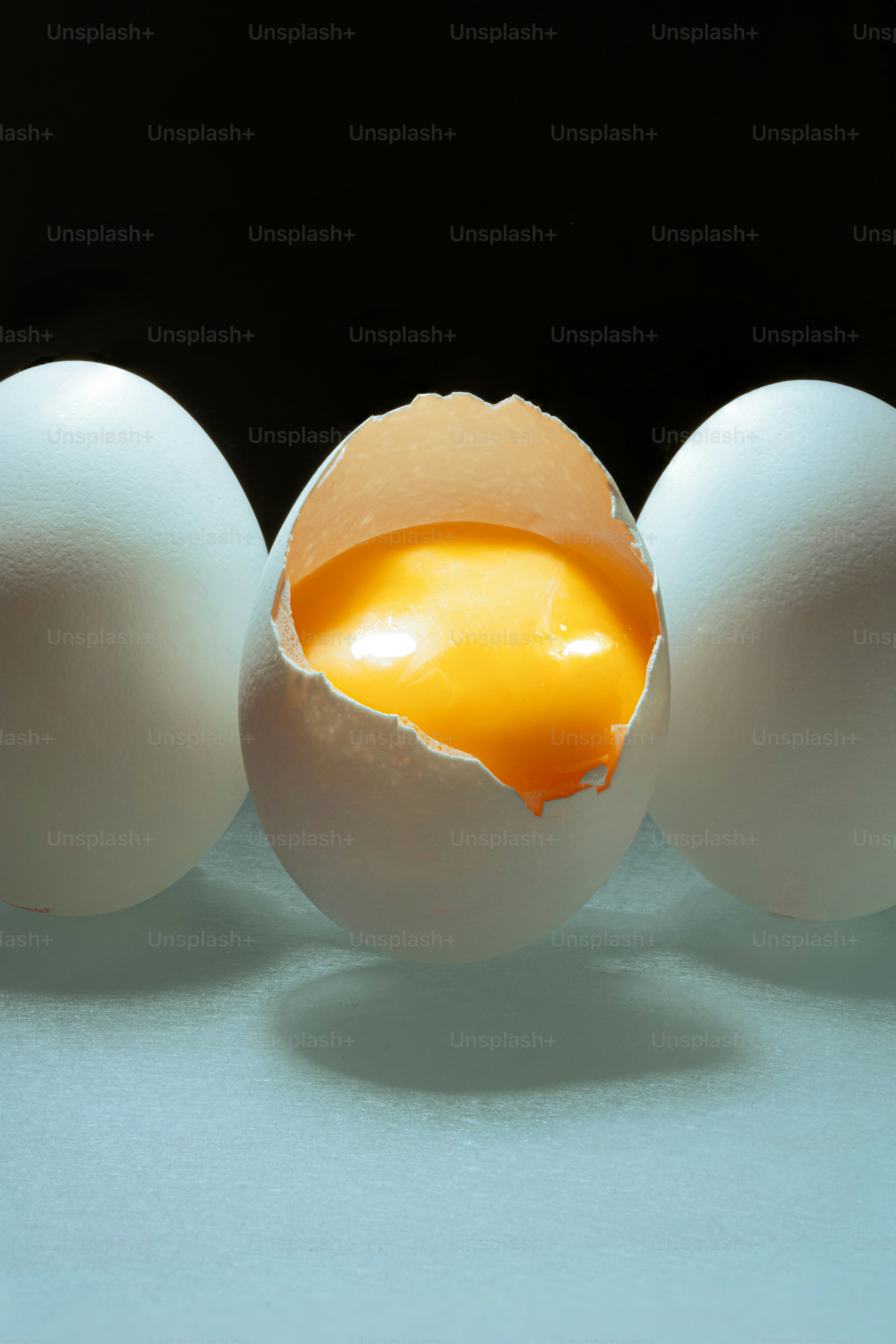 Three eggs, one cracked open with yolk visible