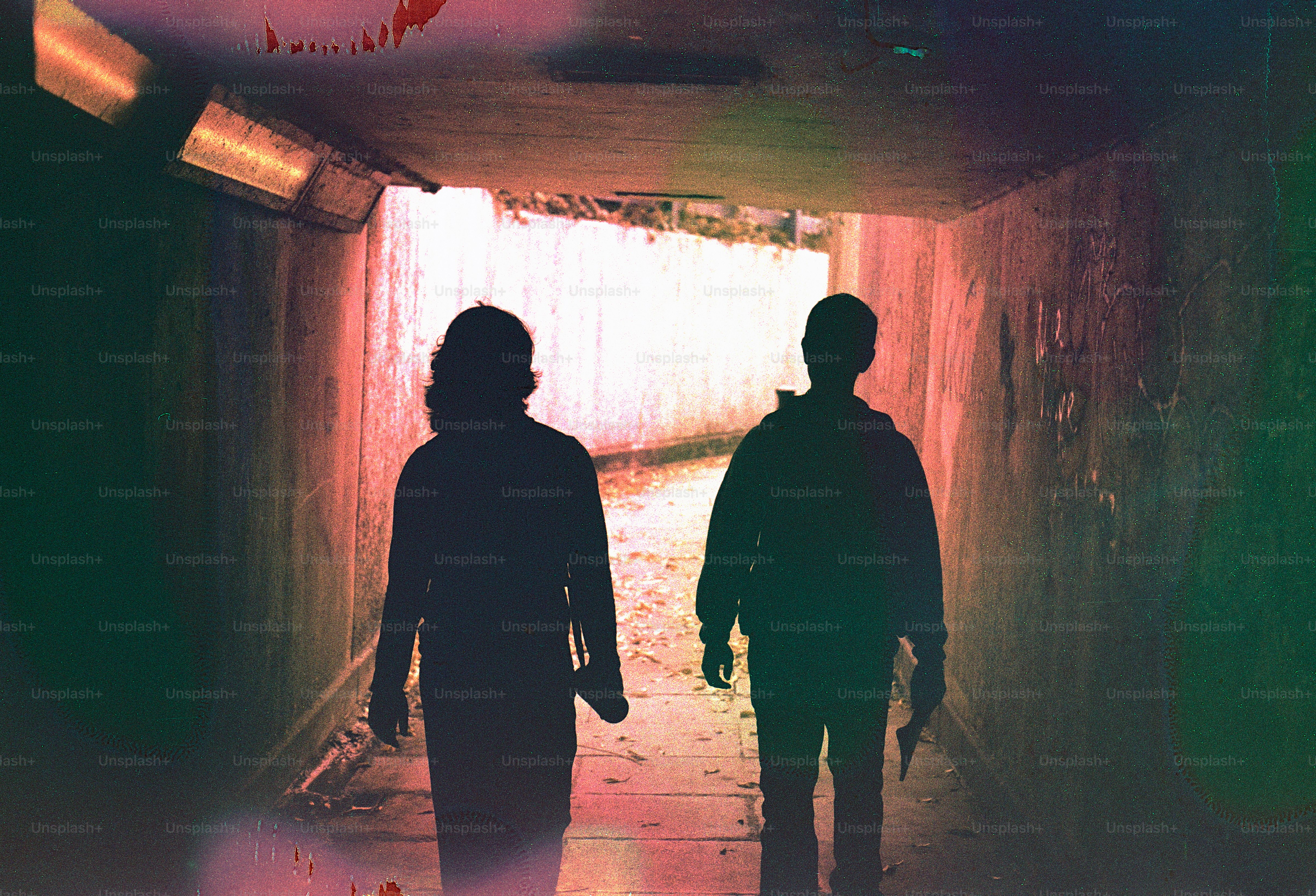 Two silhouetted figures walk through a dark tunnel.