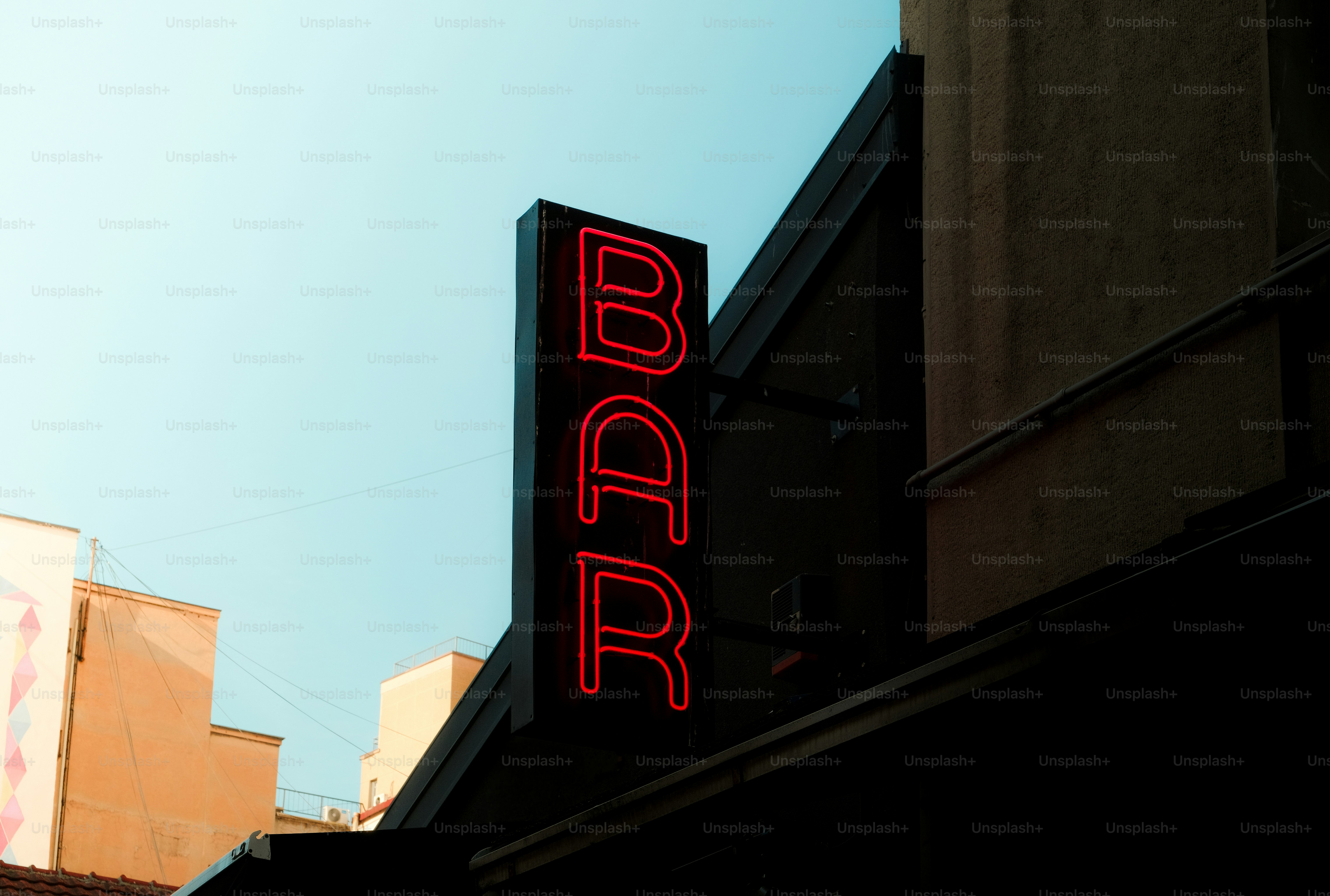 Tanda bar neon merah dengan langit biru.