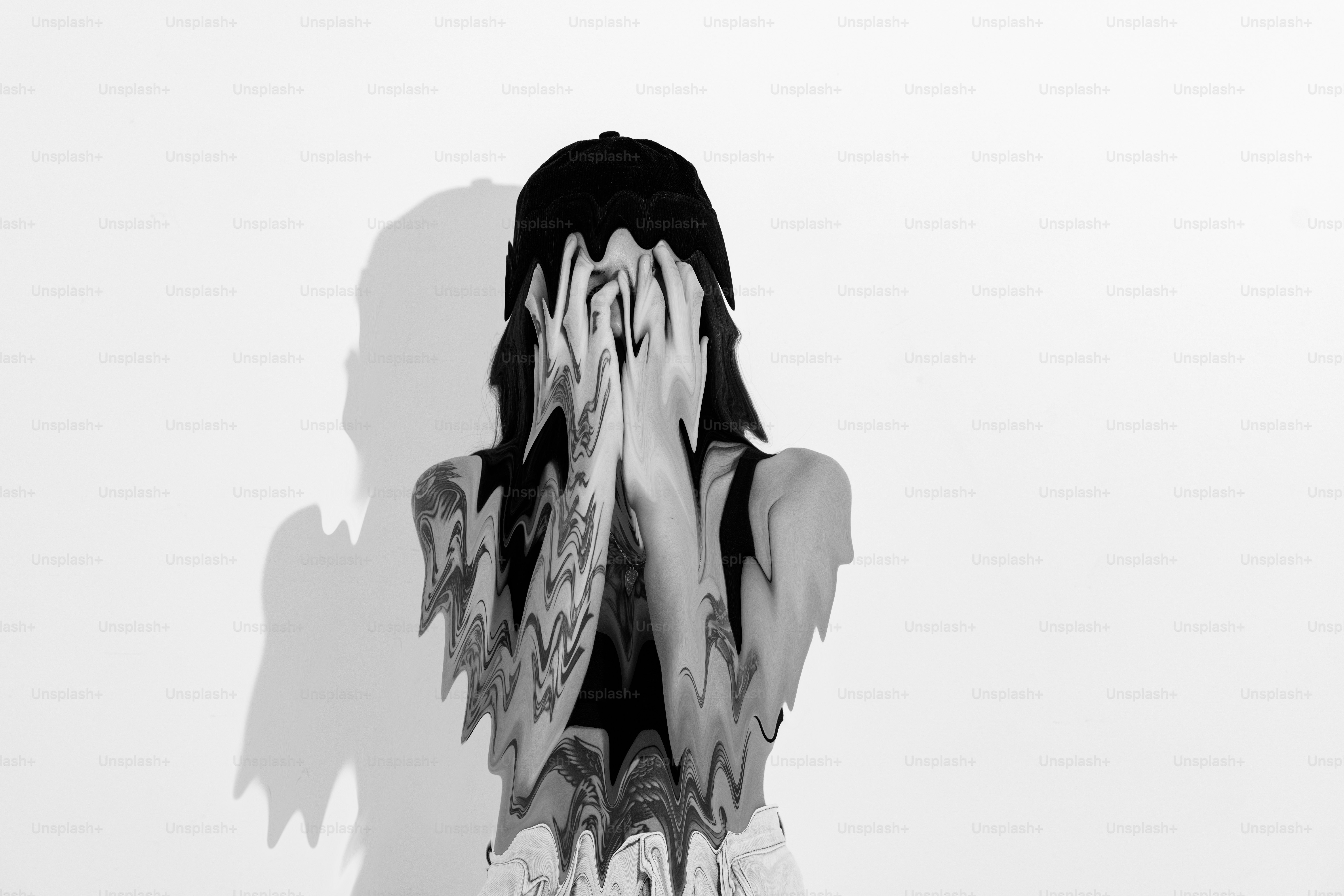 Tattooed person covers face with hands against white background.