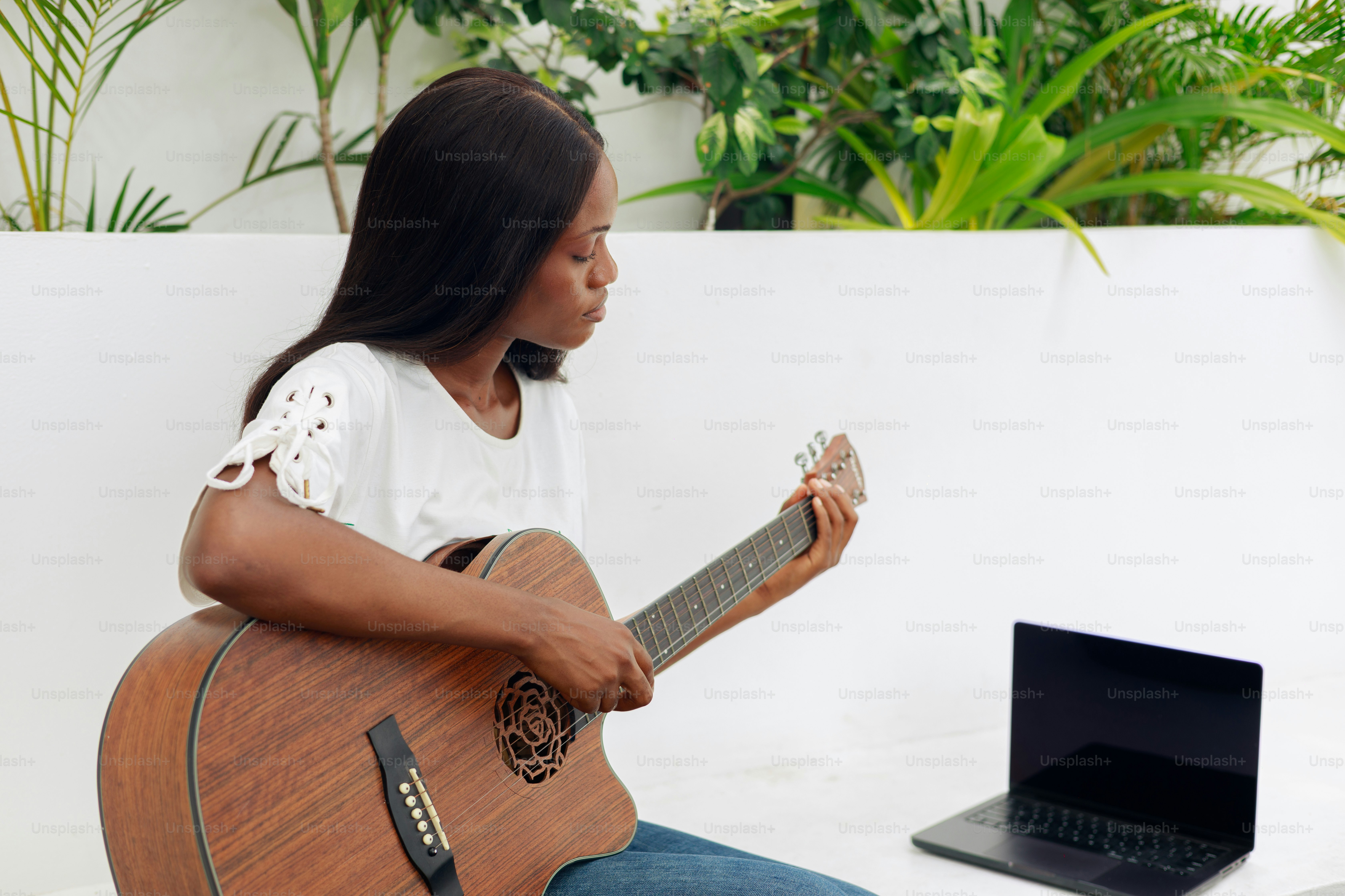 Young woman playing acoustic guitar near laptop