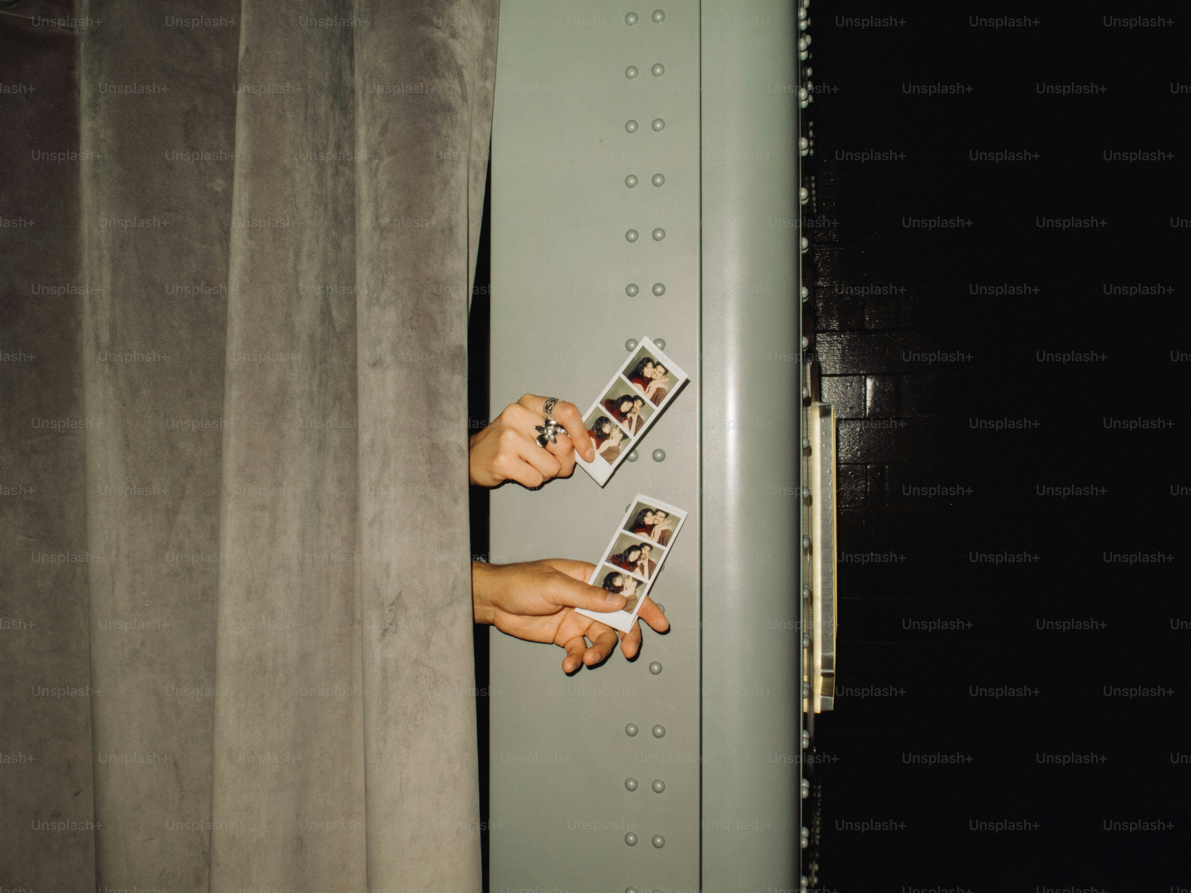 Hands holding photo booth strips inside booth