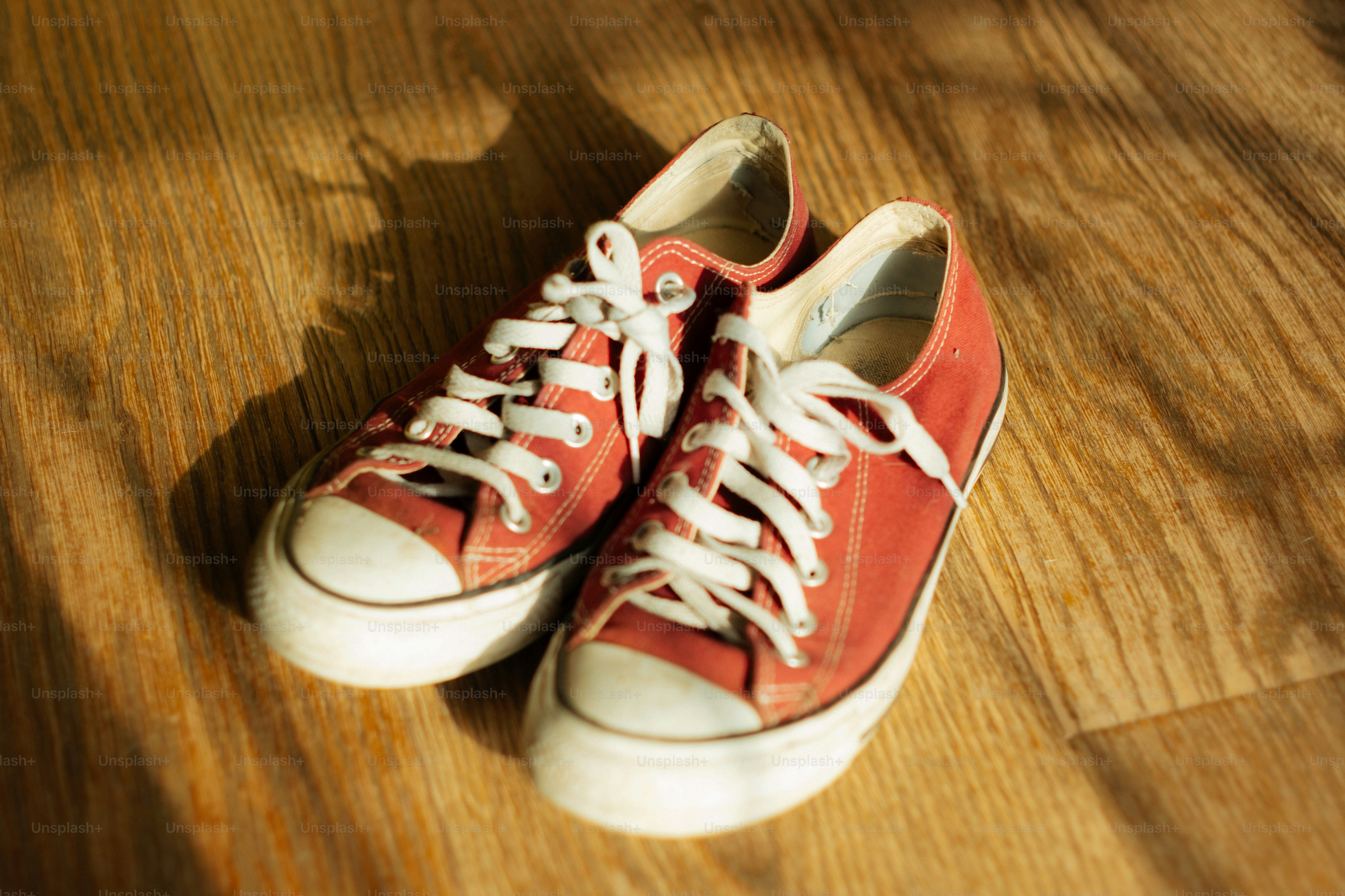 Sepasang sepatu kets kanvas merah di lantai kayu