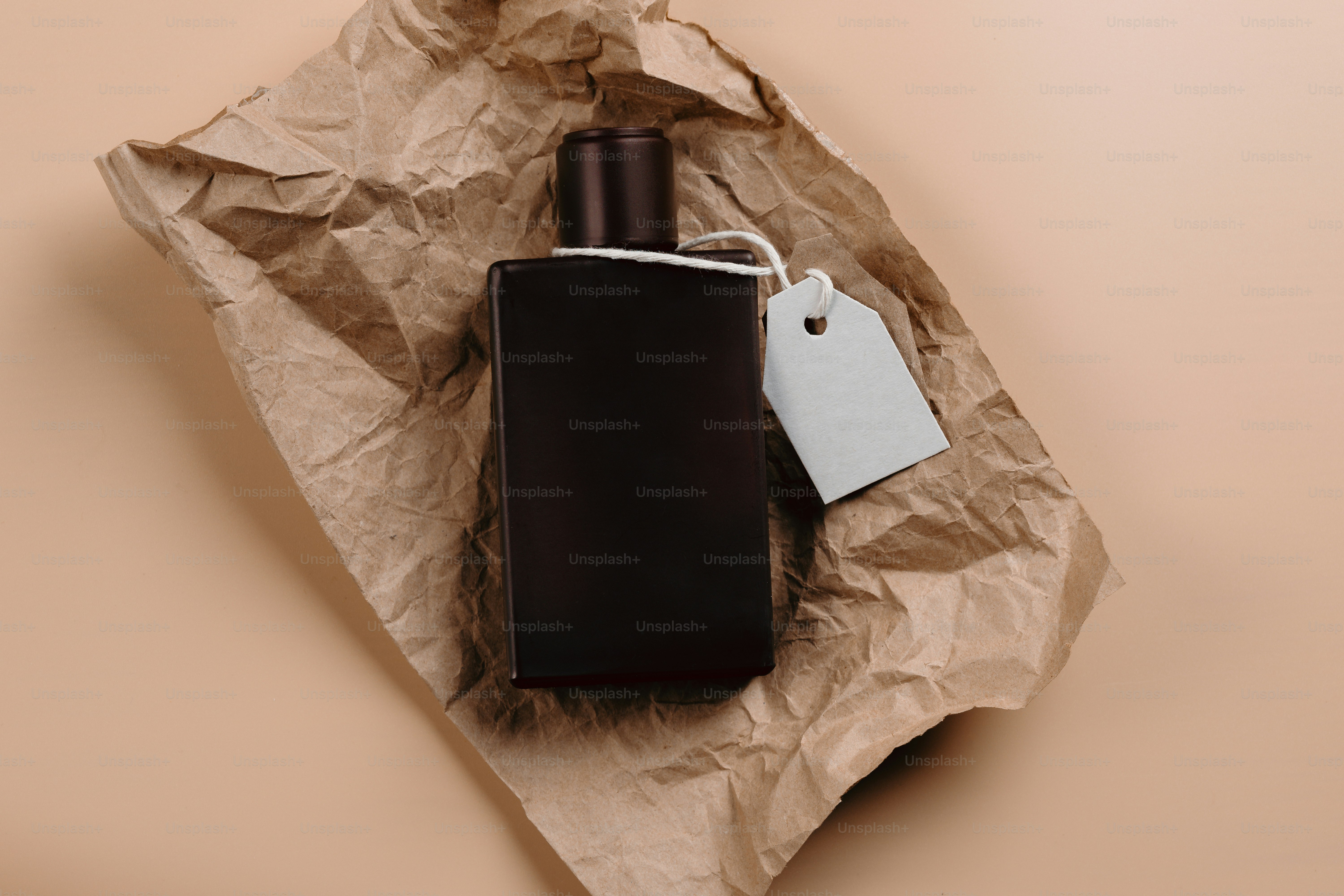 Flacon de parfum noir sur papier brun froissé.