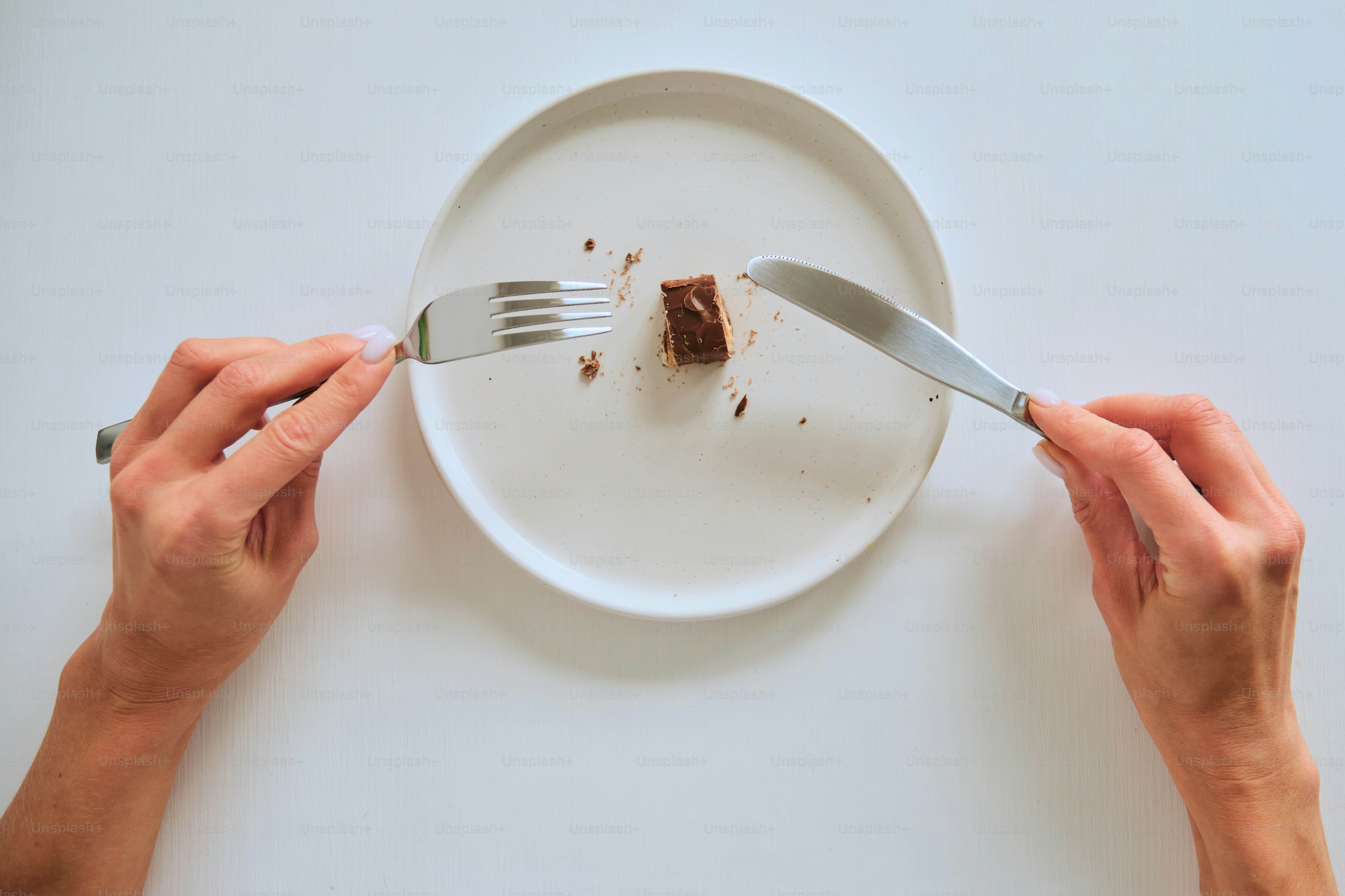 Mains coupant un petit morceau de chocolat sur une assiette.