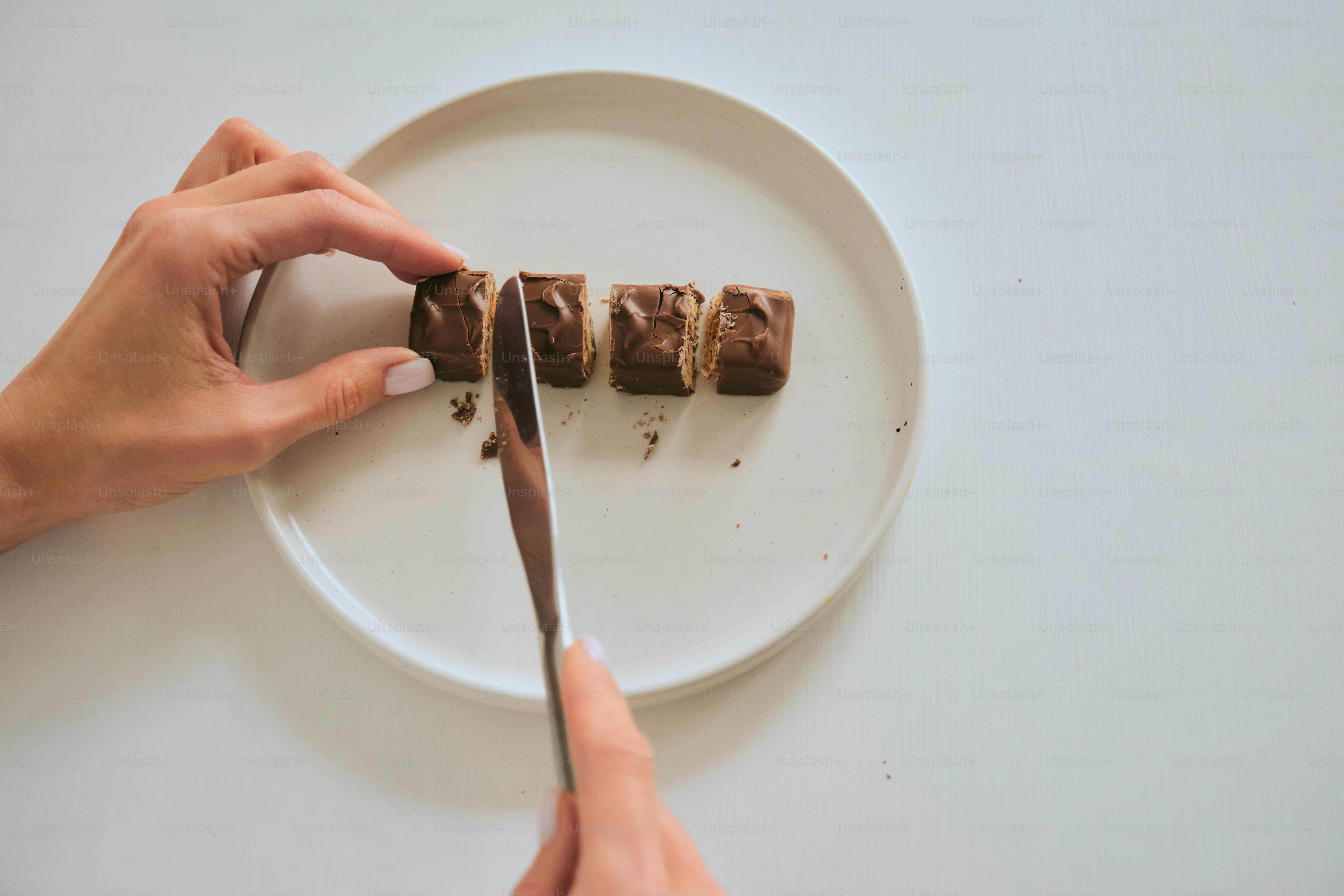 Hände, die Schokoriegel auf einem weißen Teller schneiden