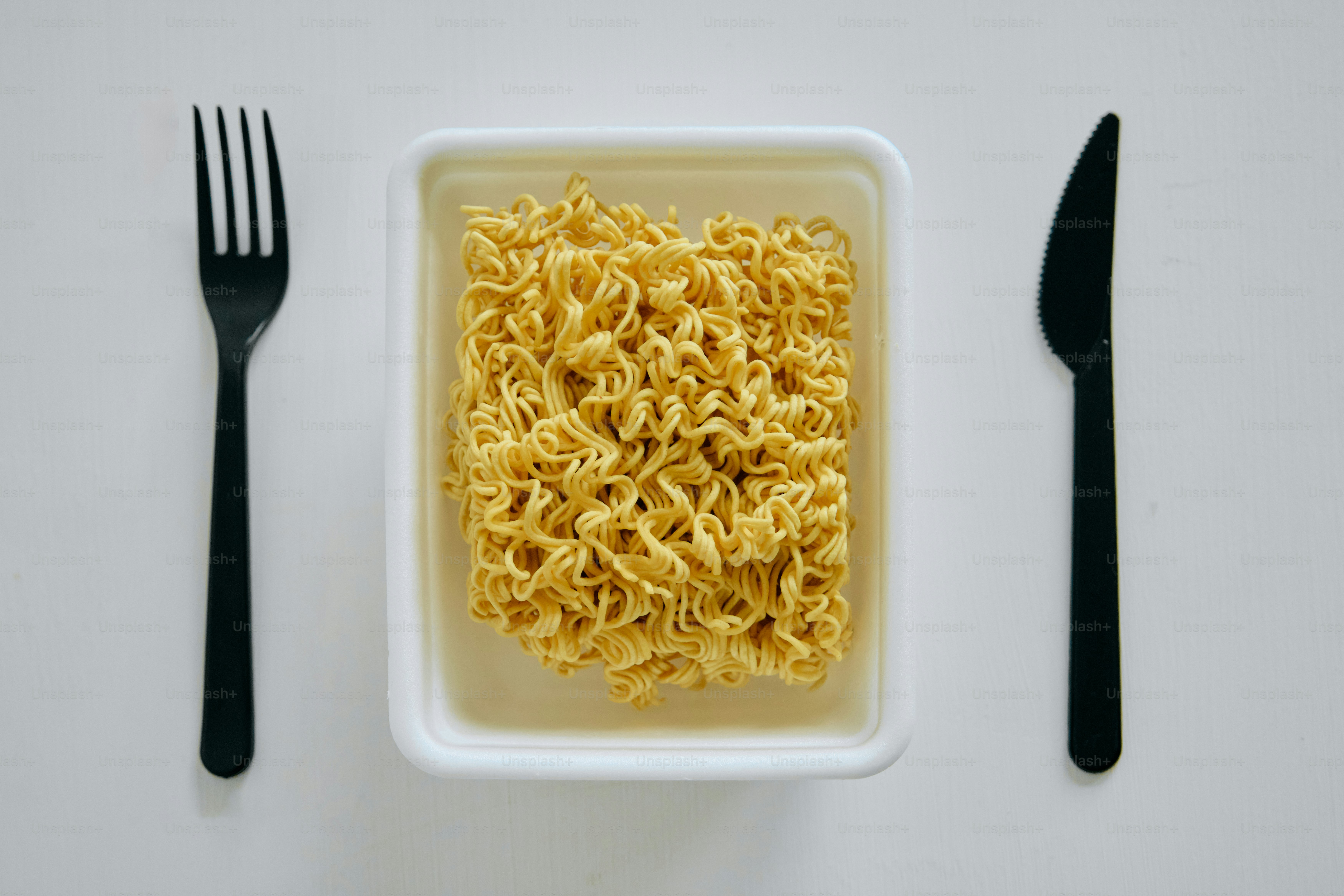 Instant noodles in a white container with cutlery.