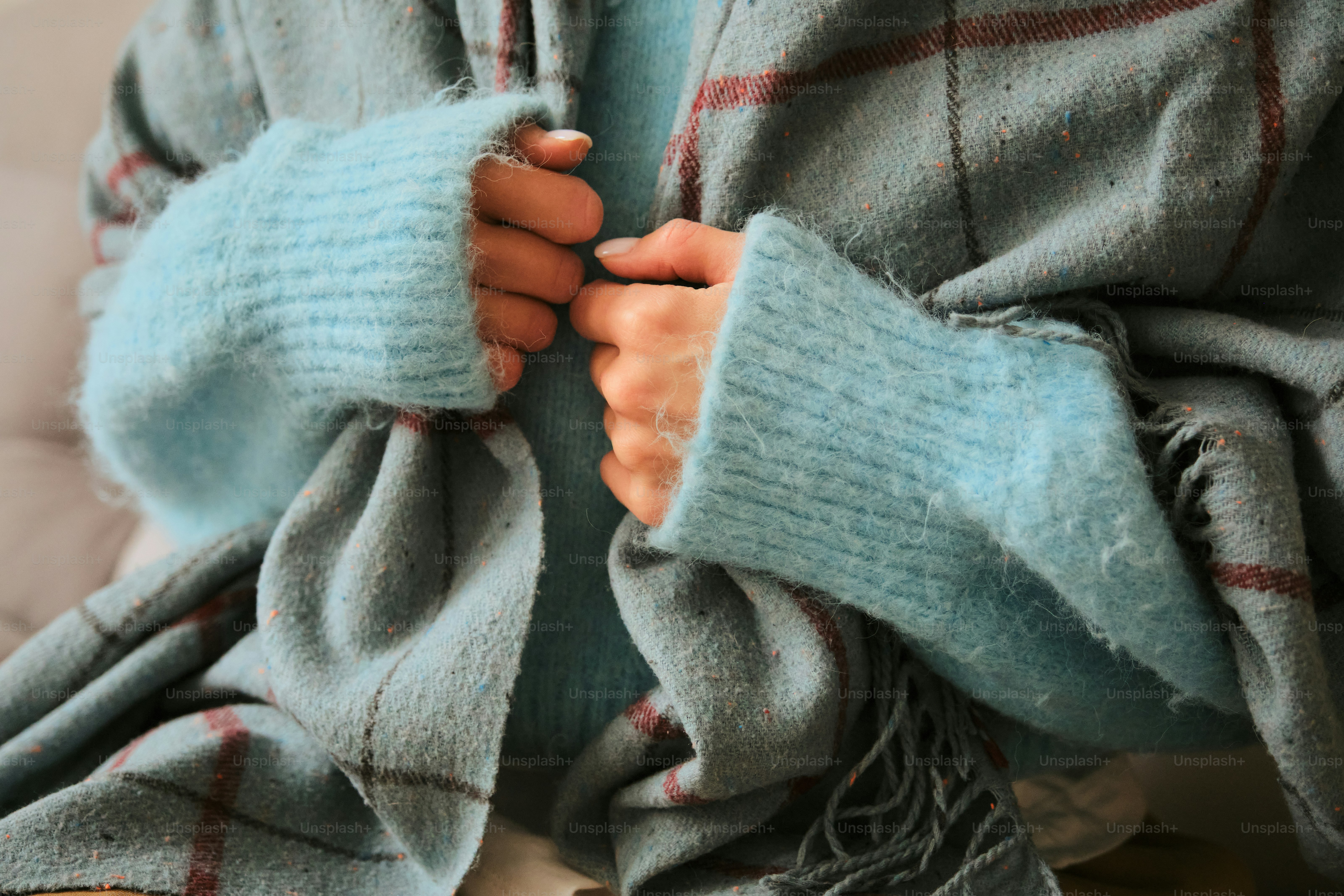 Person, die sich in einen kuscheligen Pullover und eine Decke einwickelt.