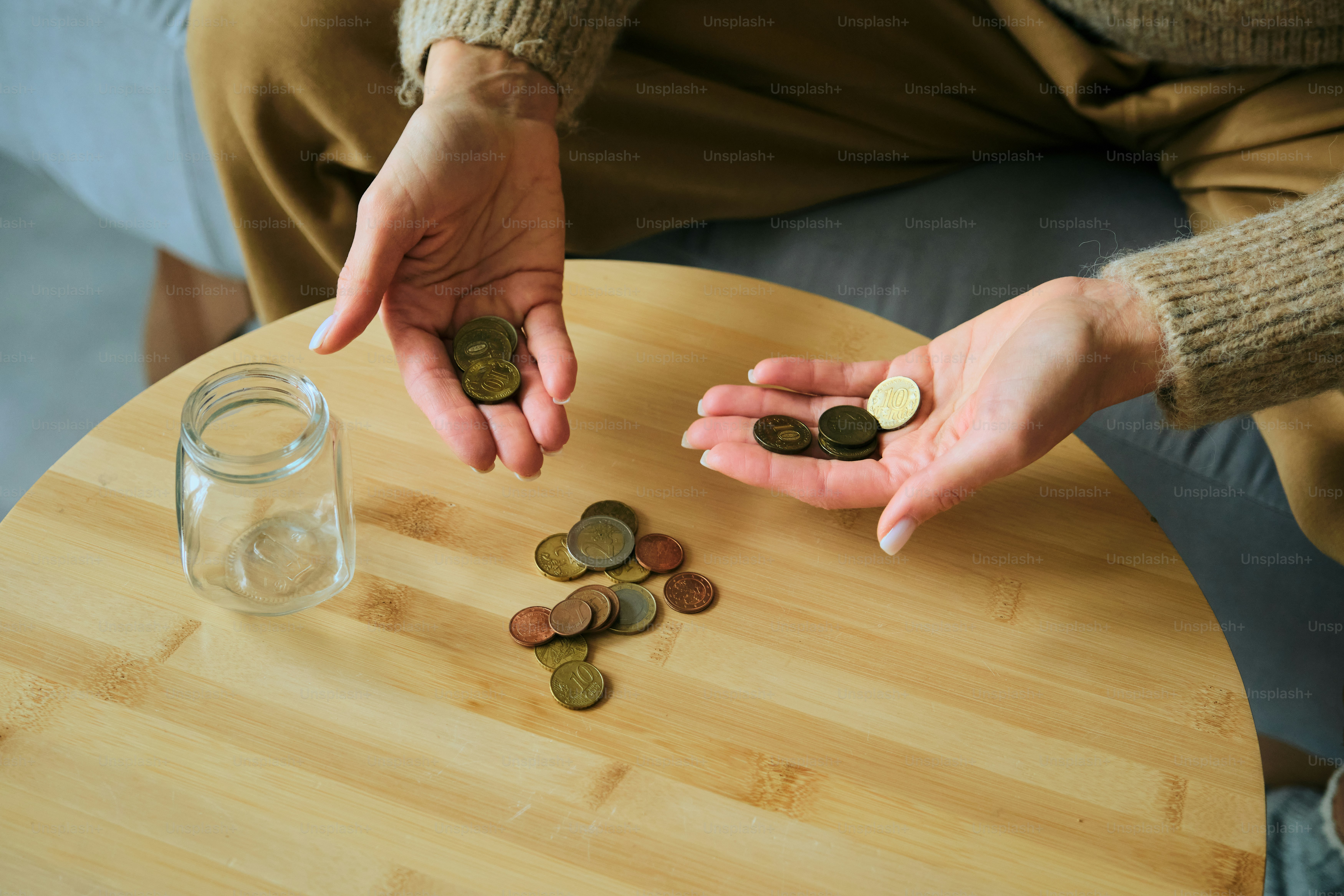 Hände, die Münzen zählen, neben einem Glas auf einem Tisch