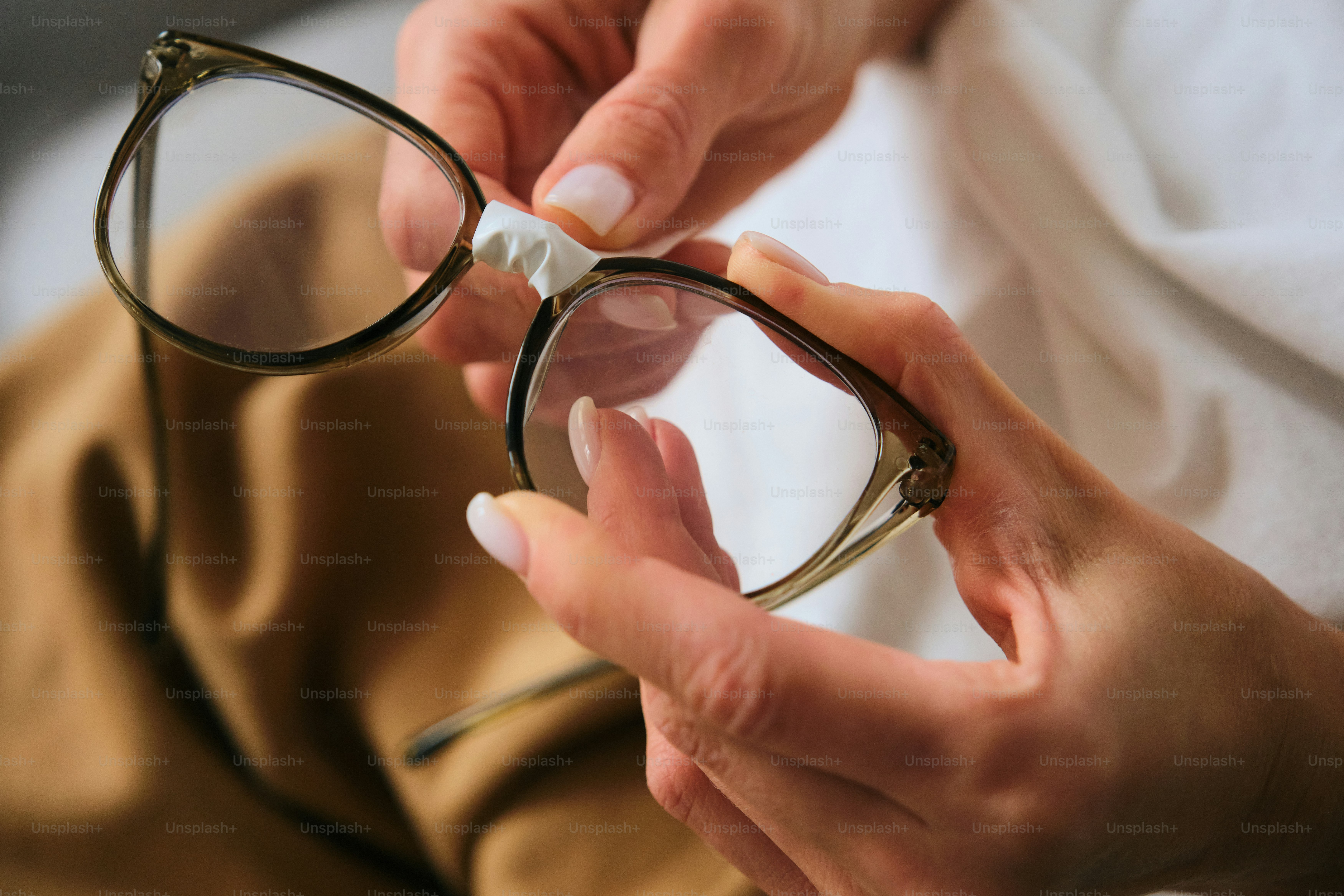 Hands cleaning eyeglasses with a cloth.