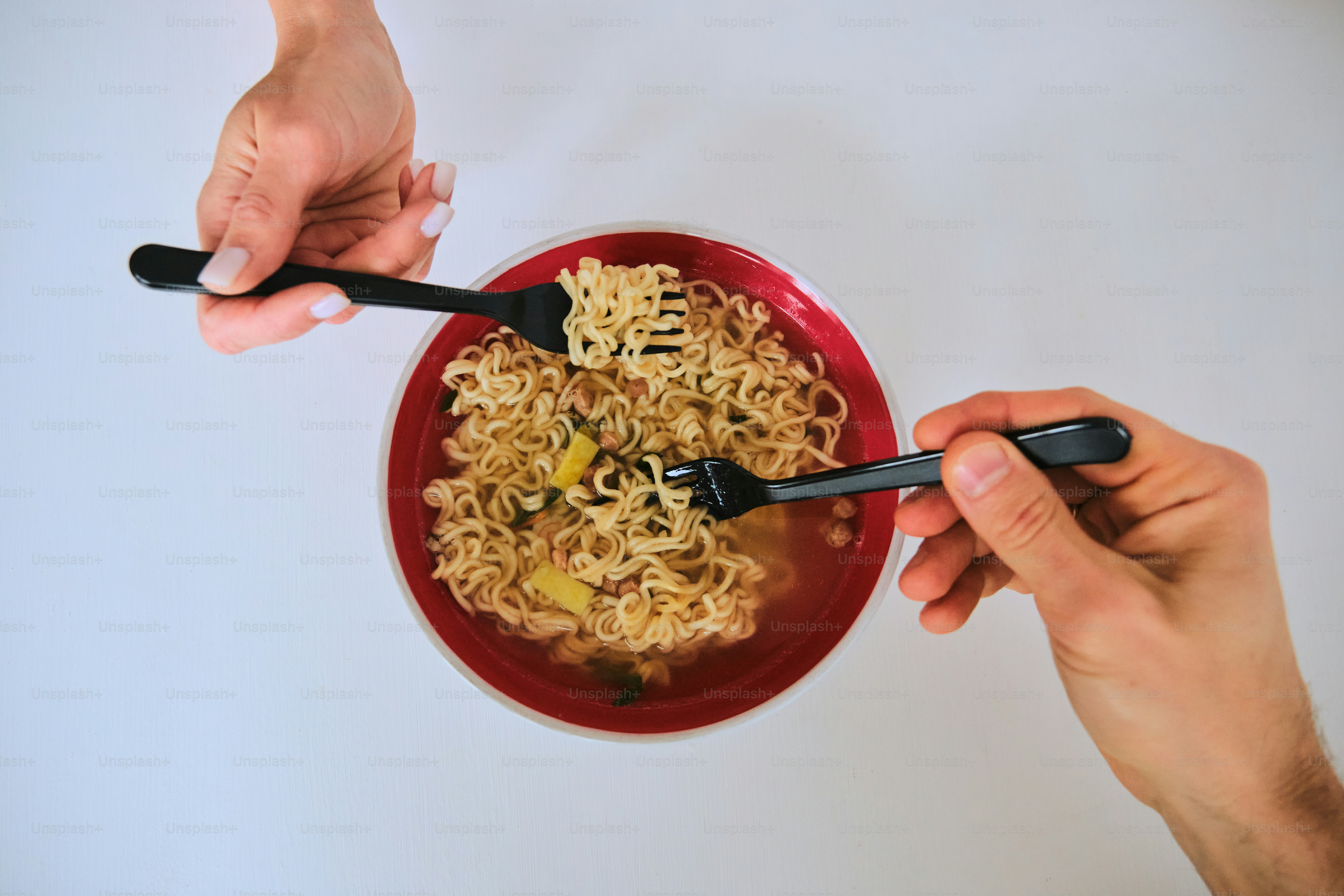 Two hands using forks to eat ramen noodles