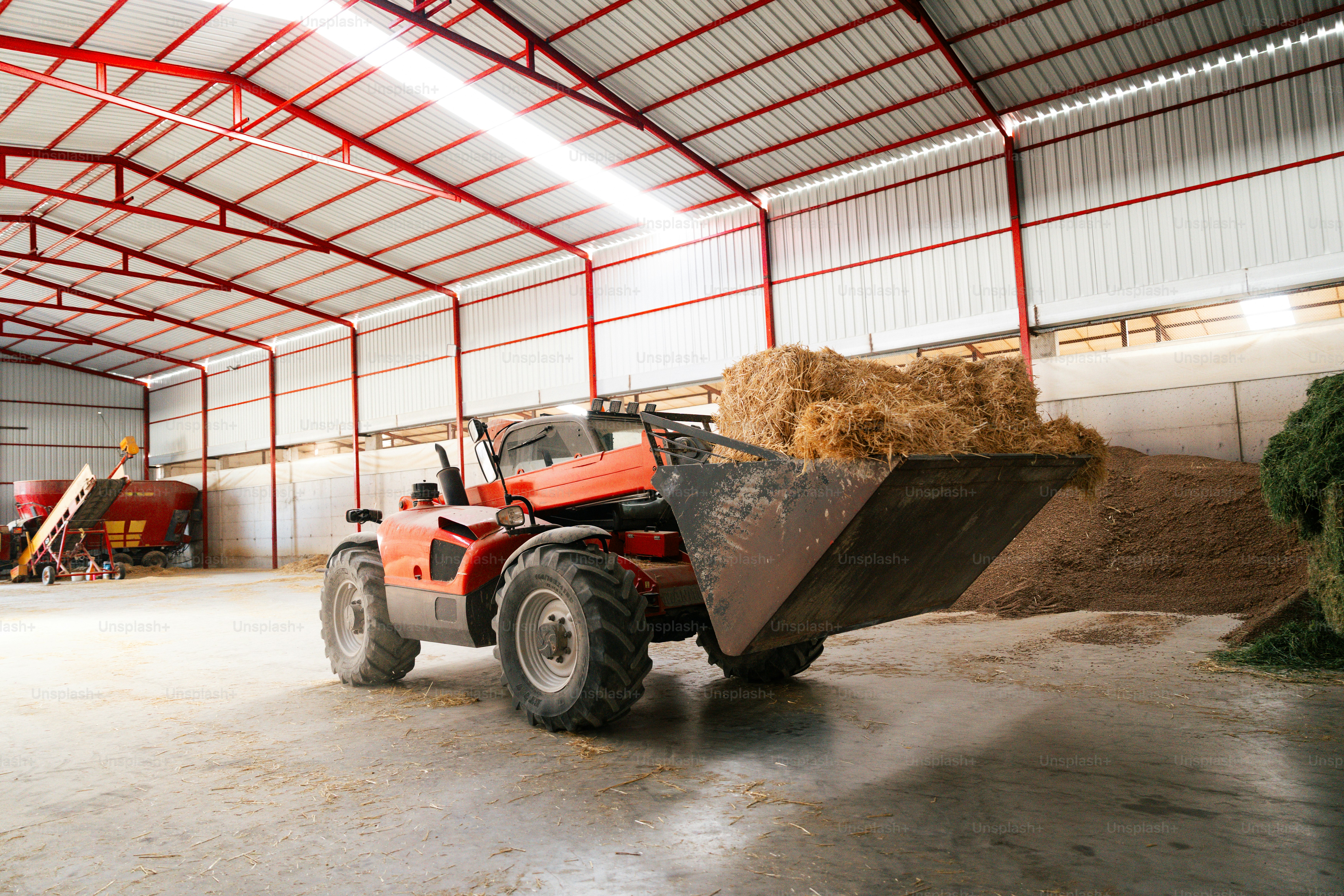 Forklift loading hay bales inside a large barn.