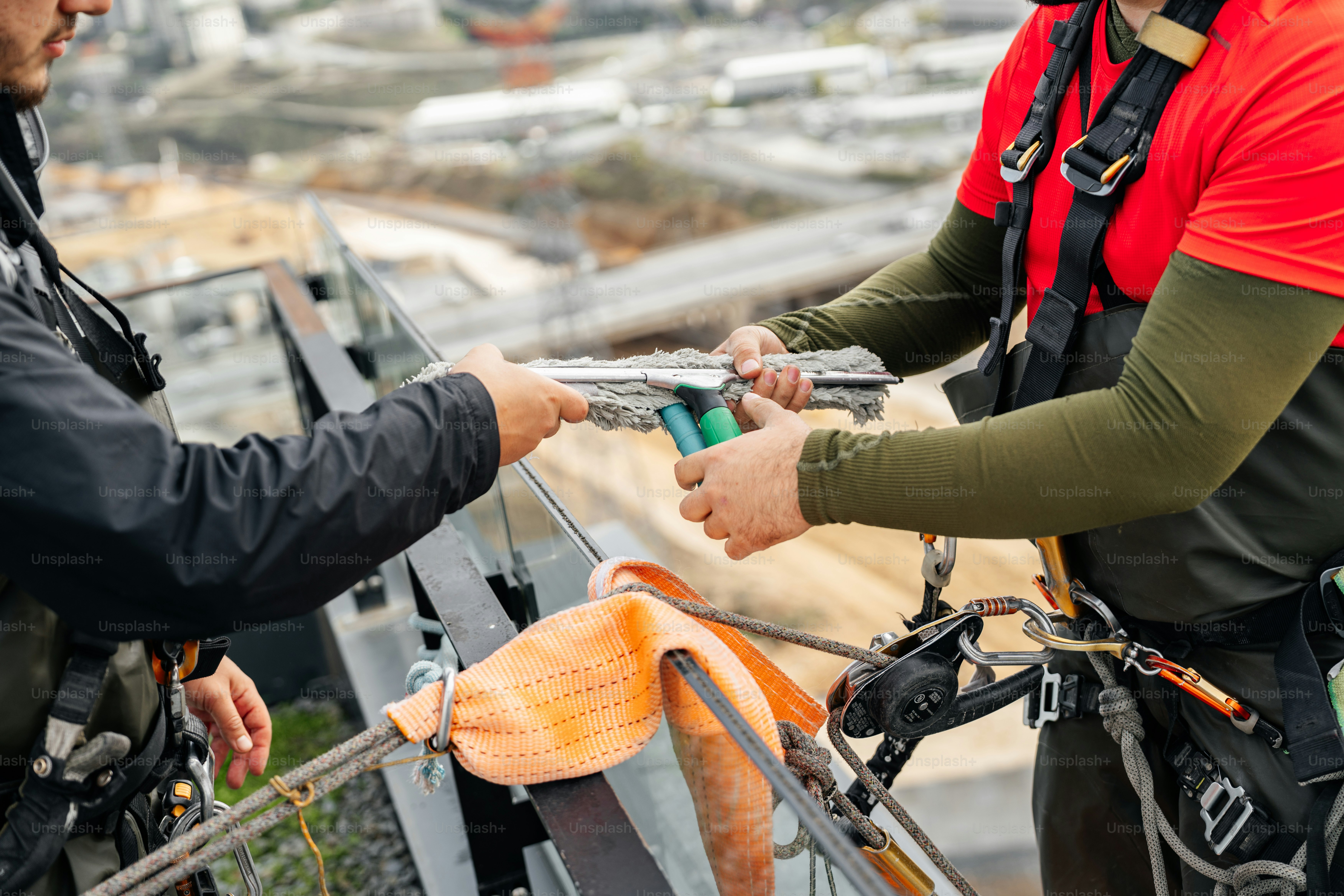 Two construction workers on a high-rise building exchange items.
