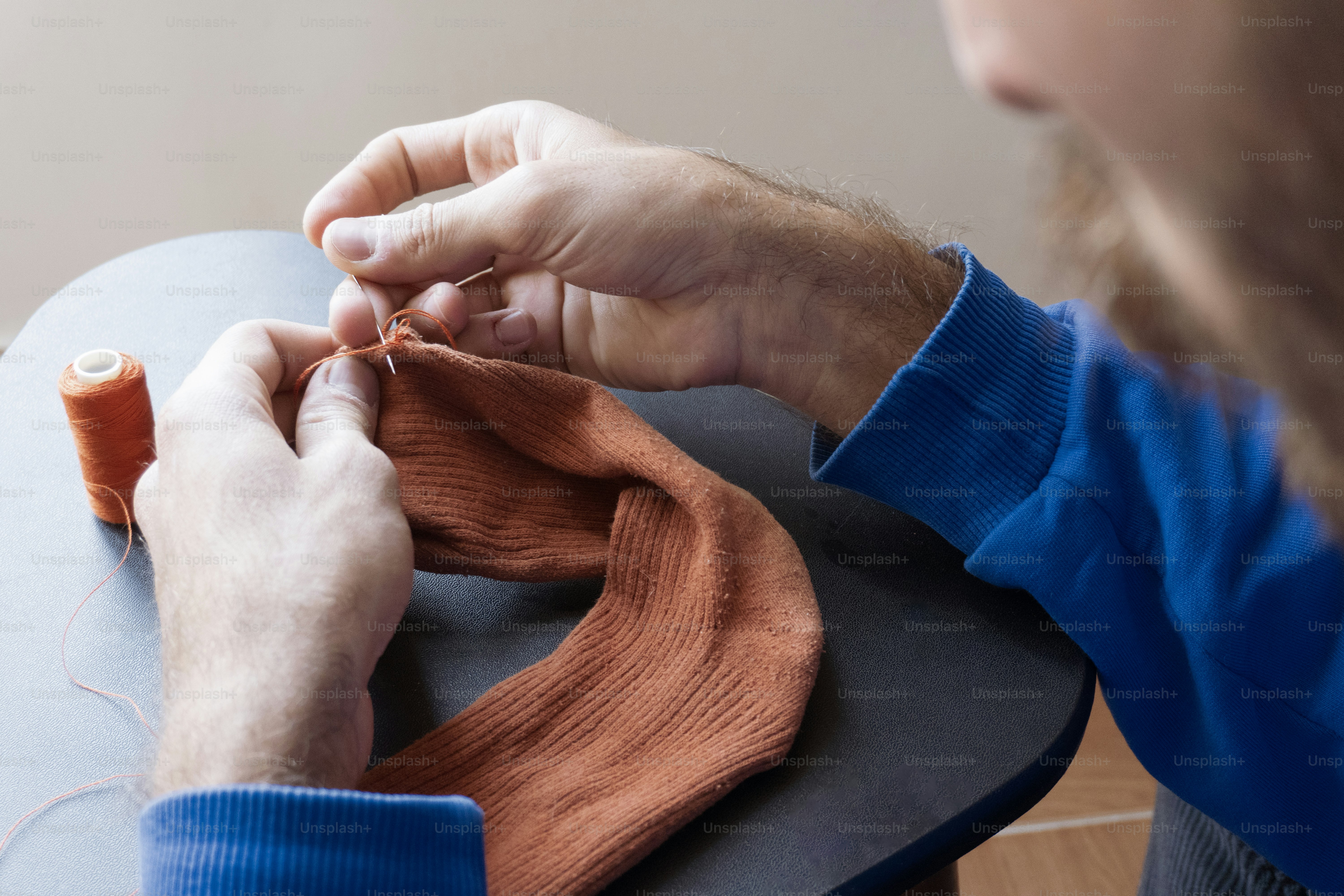 Man sewing an orange sock with orange thread.