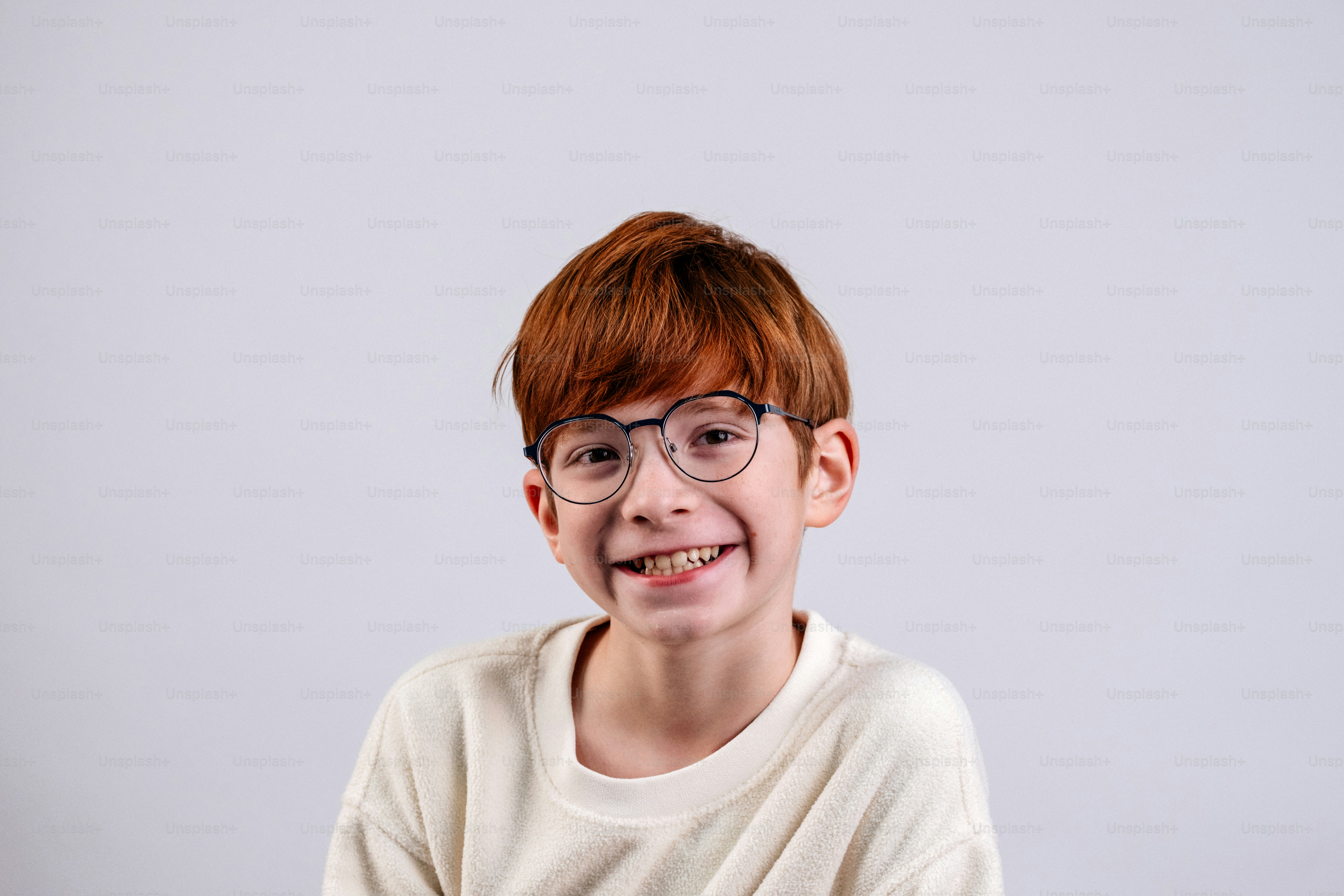 Giovane ragazzo con i capelli rossi e gli occhiali sorride ampiamente sorridente.