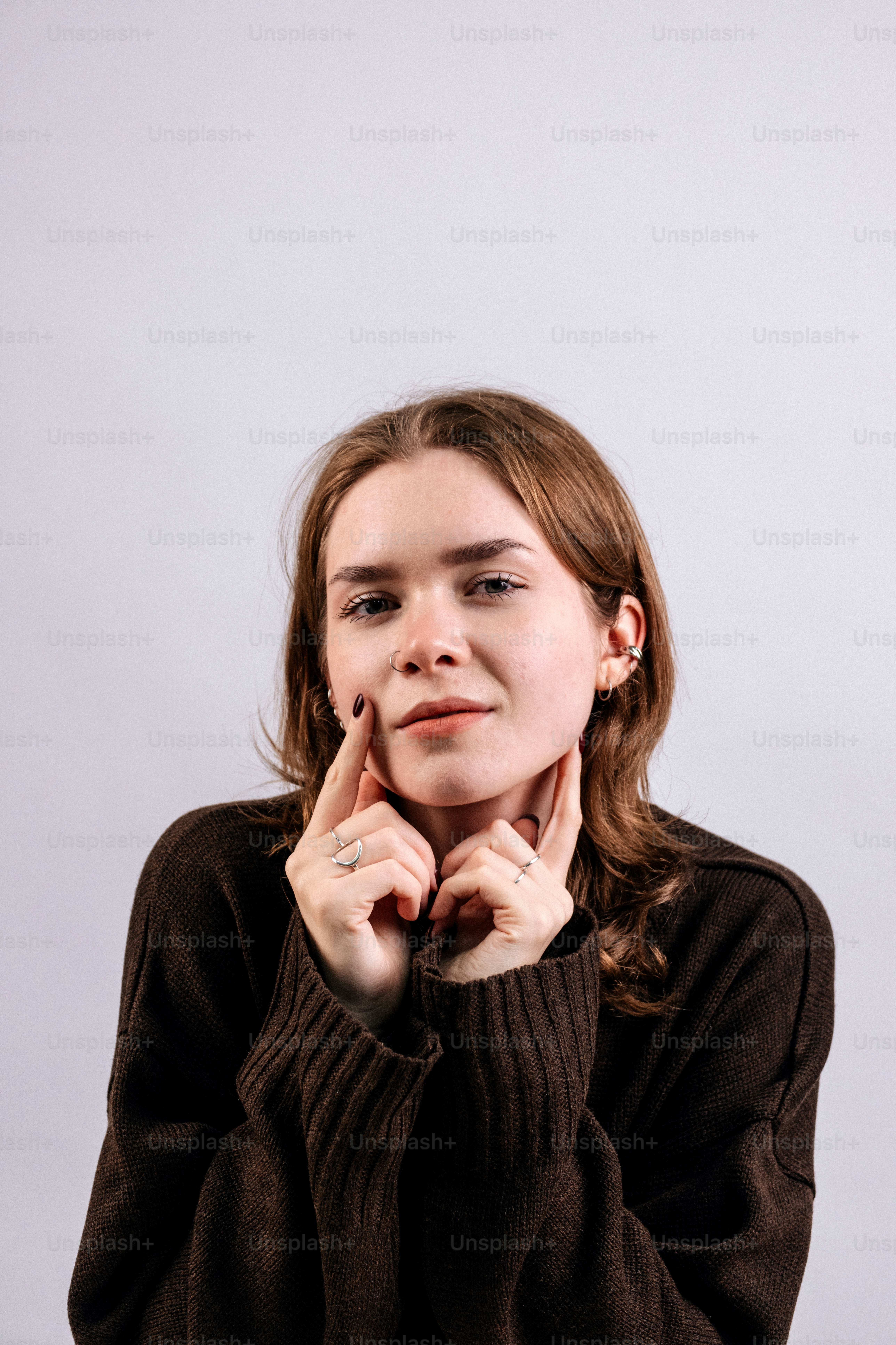 Young woman with fingers on cheeks, wearing a brown sweater.