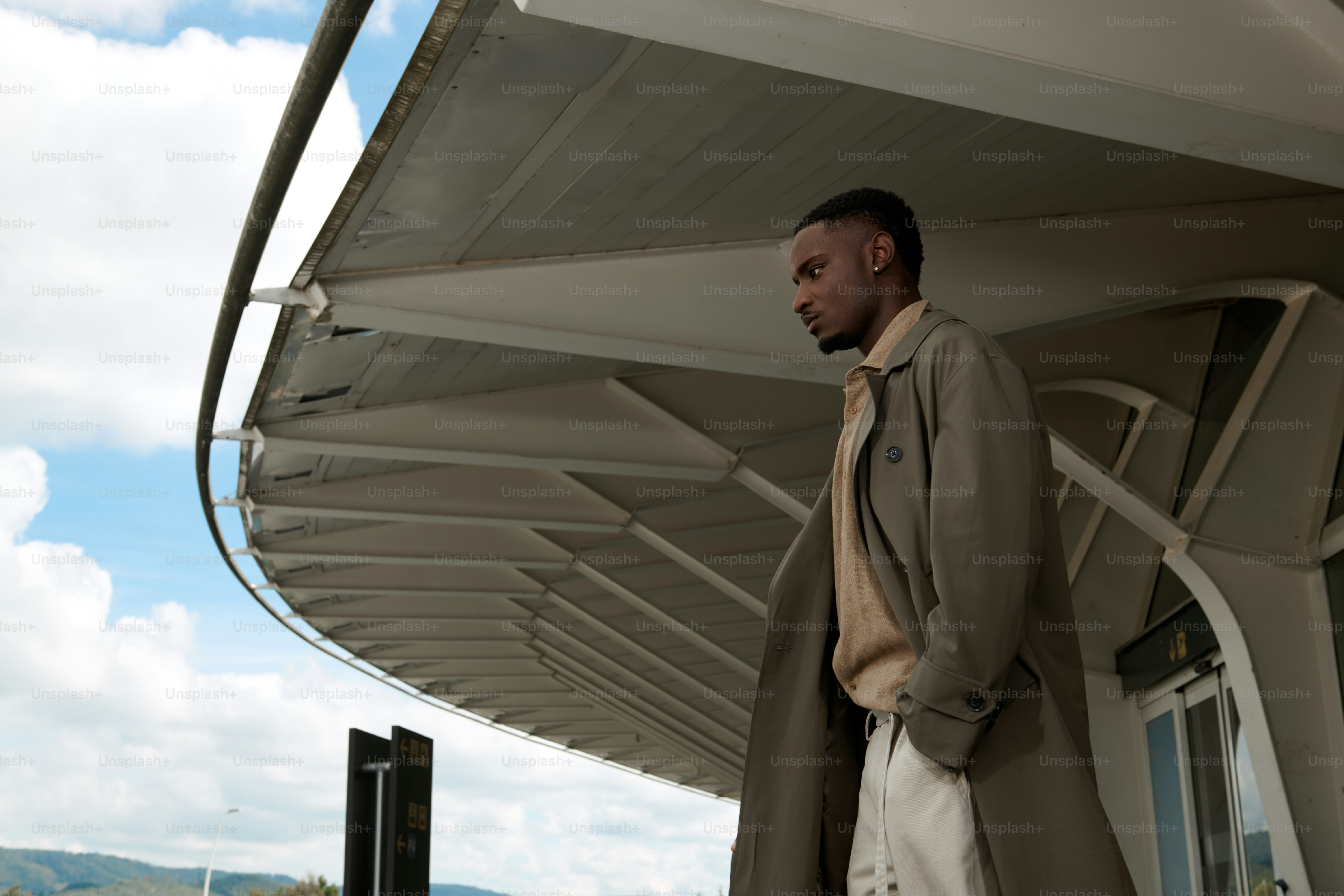Man in trench coat standing under modern architecture.