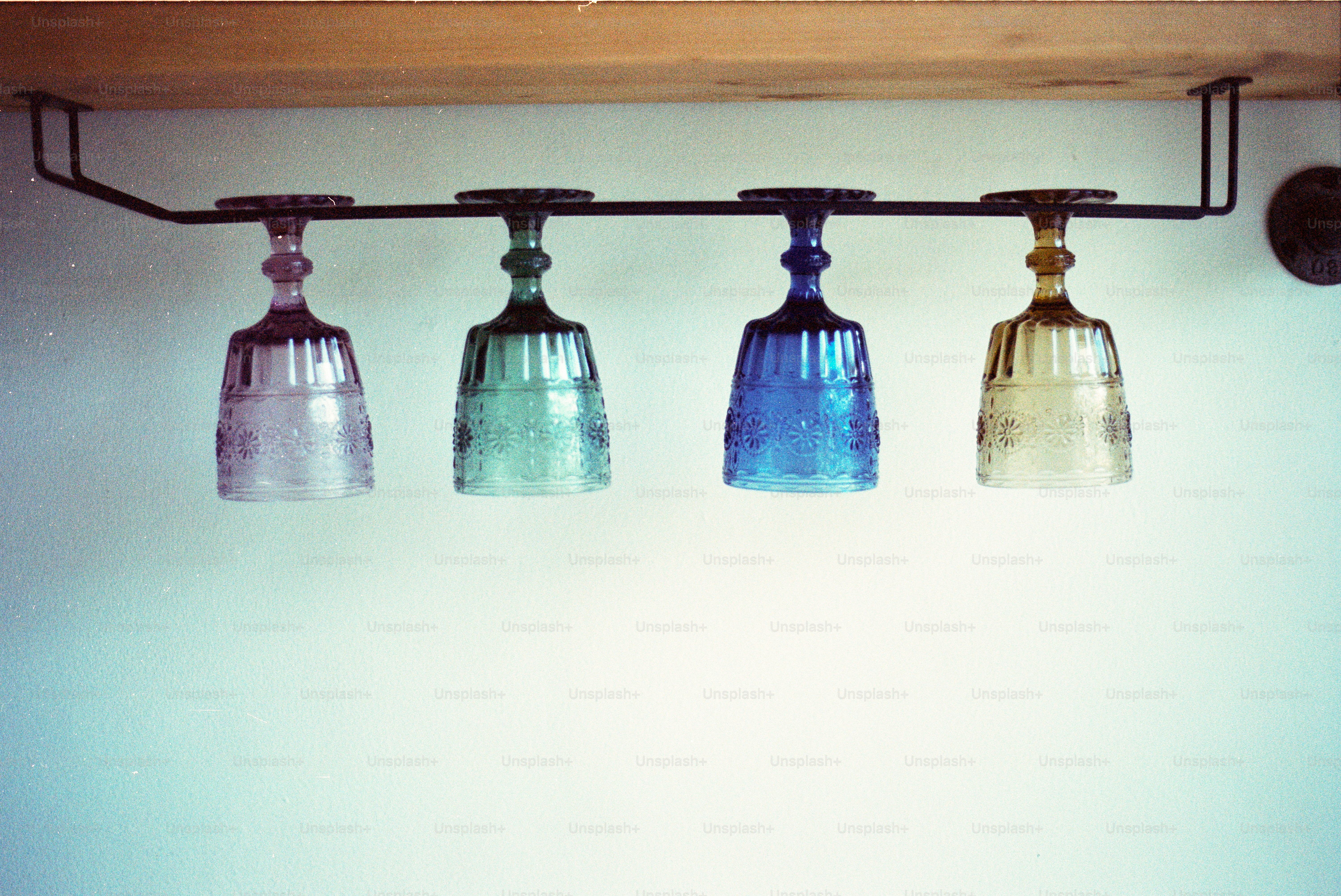 Cuatro copas de vino de colores colgando de un estante