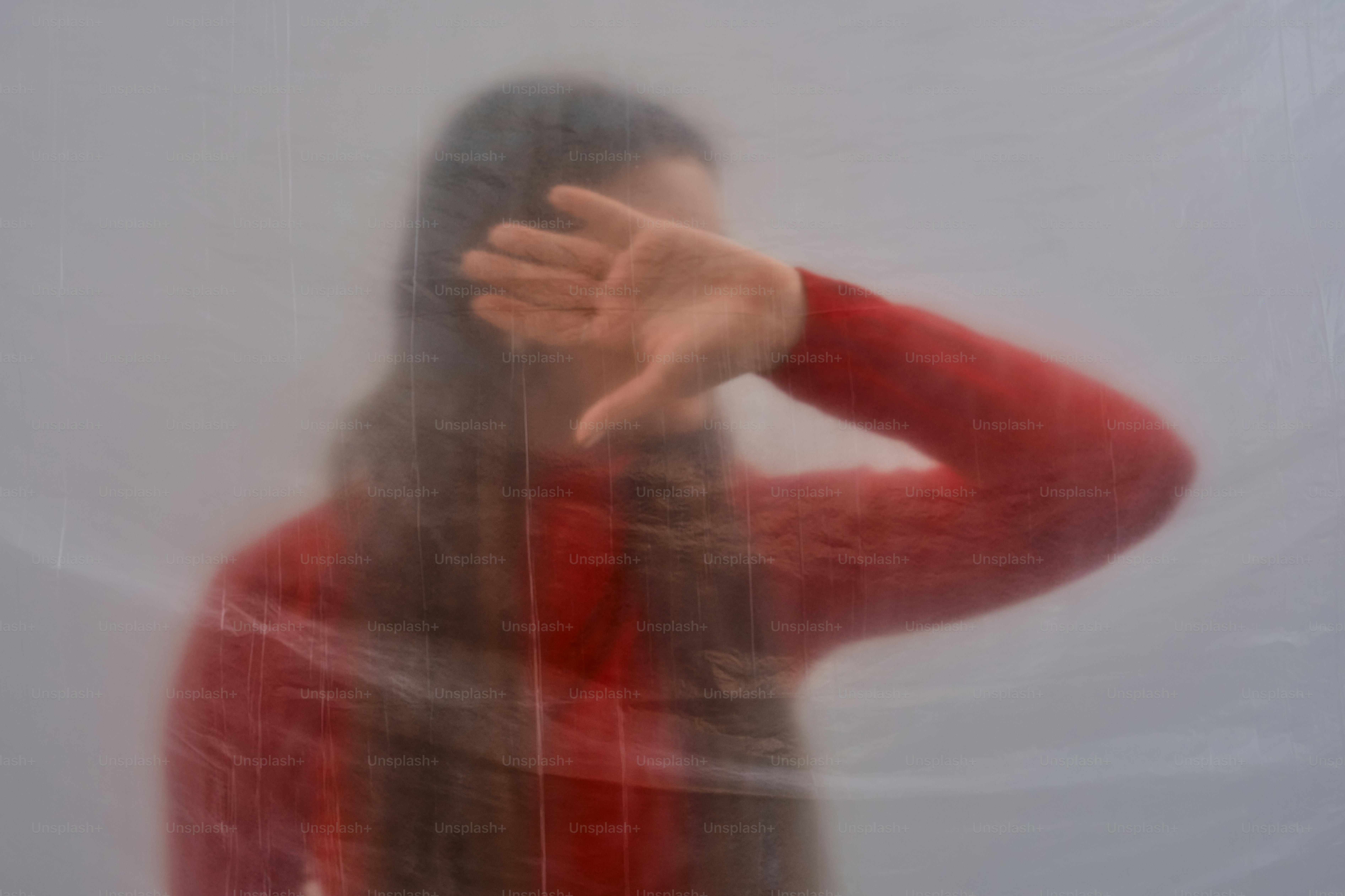 Woman in red shirt shielding face with hand.