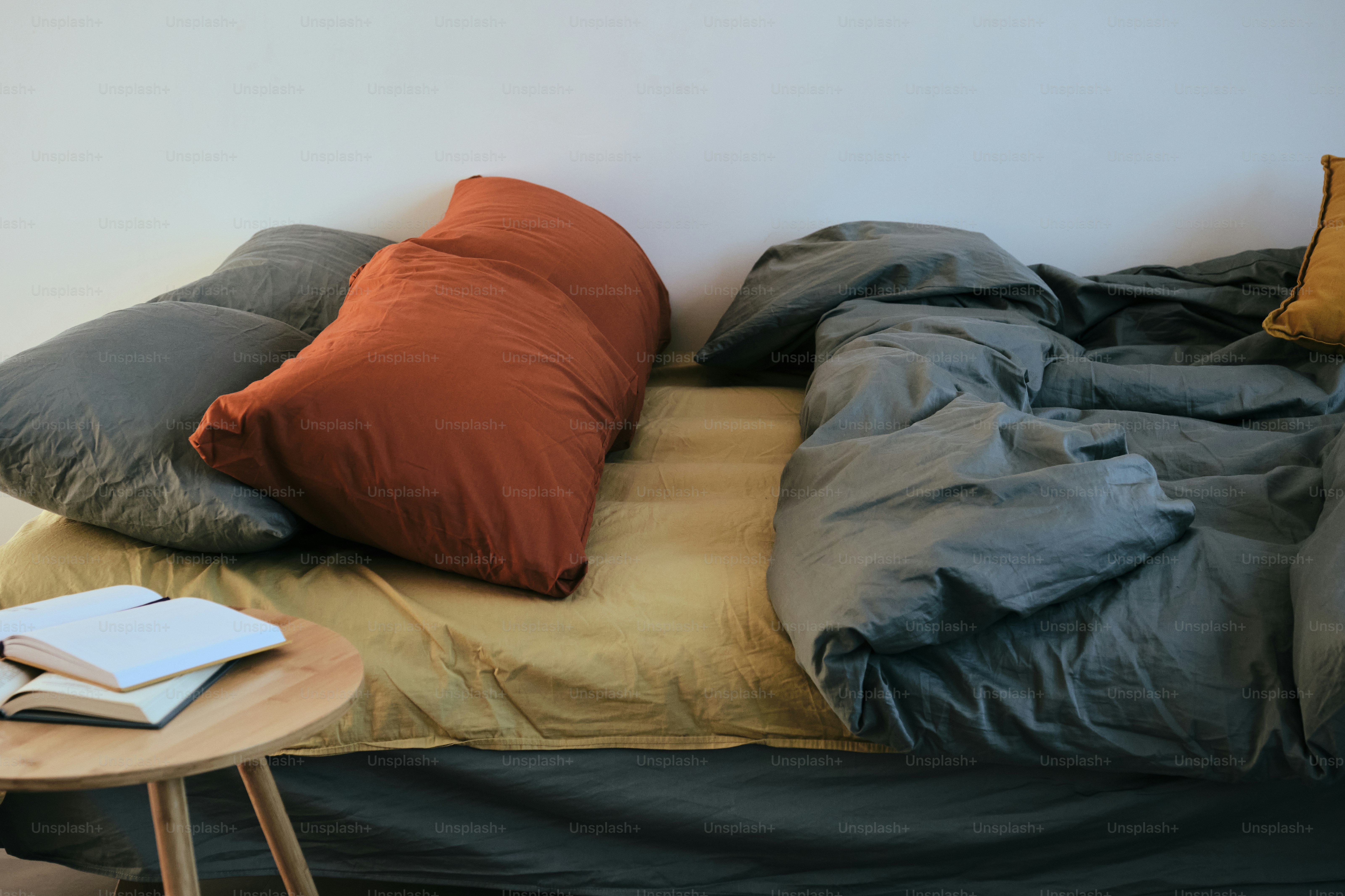 Bed with pillows, blanket, and books on table.