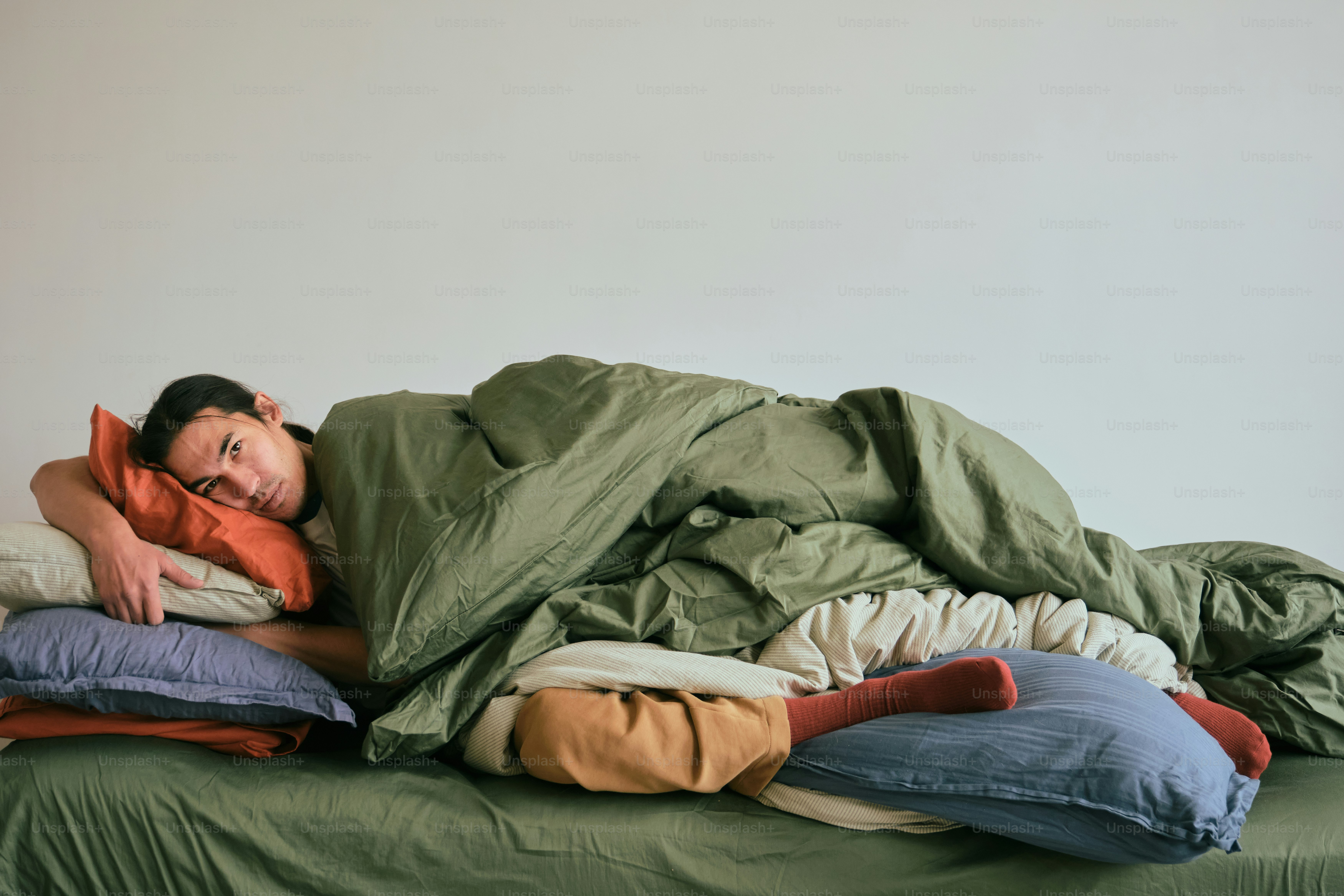 Pria tidur di tempat tidur yang ditutupi selimut dan bantal.