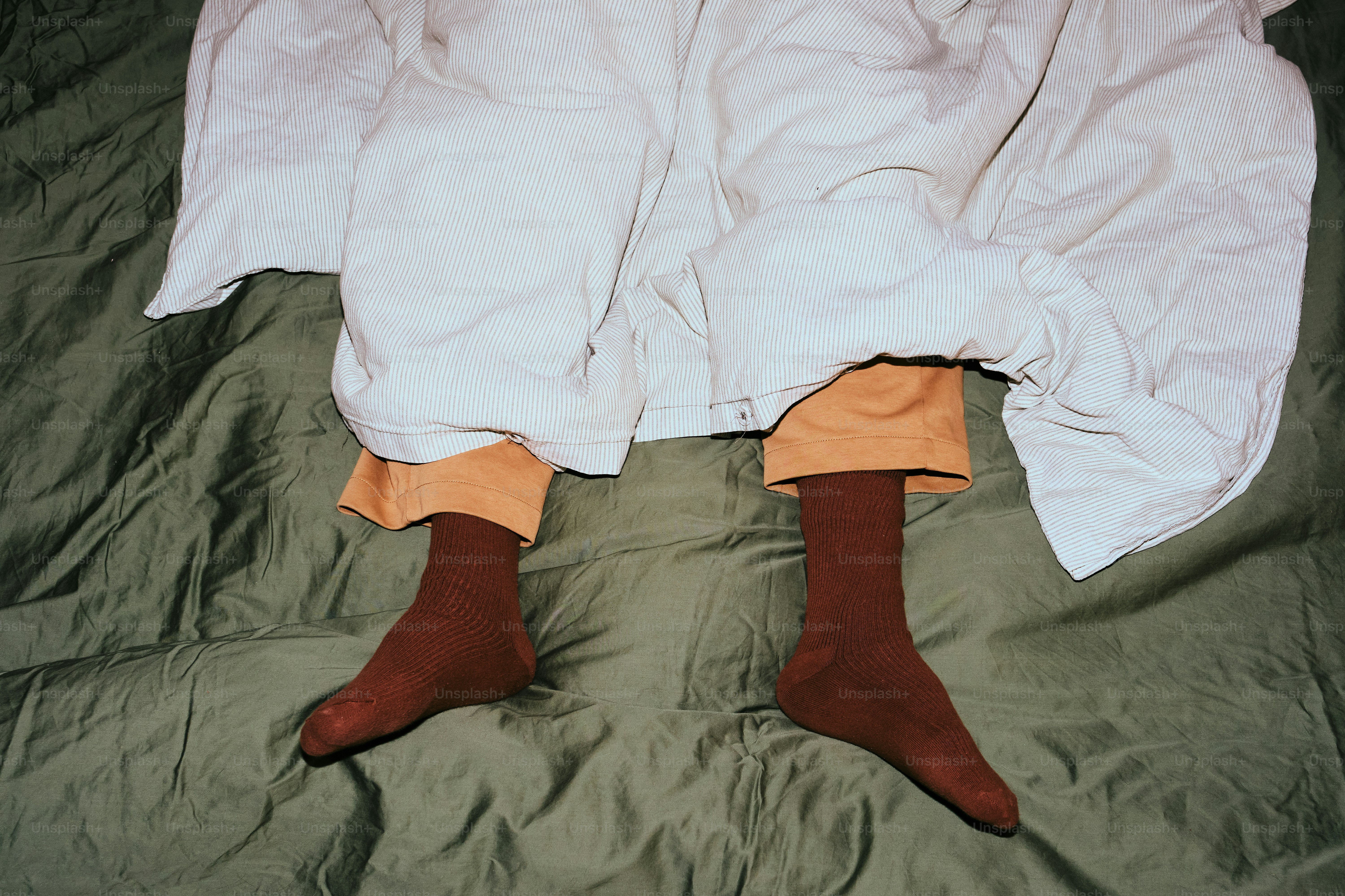 침대 위에서 흰 담요 아래 갈색 양말을 신은 발