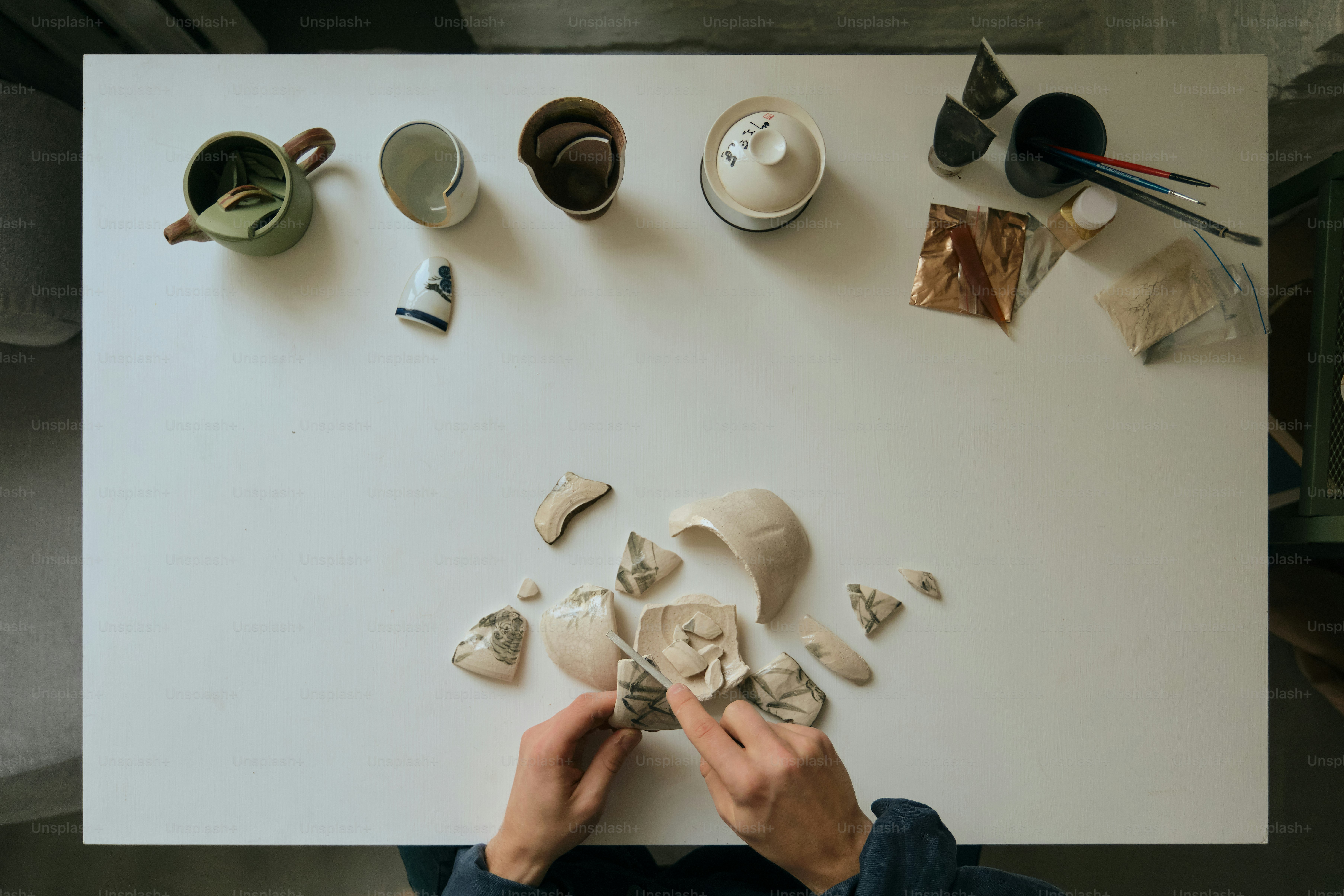 Tangan merakit potongan tembikar yang rusak di atas meja putih