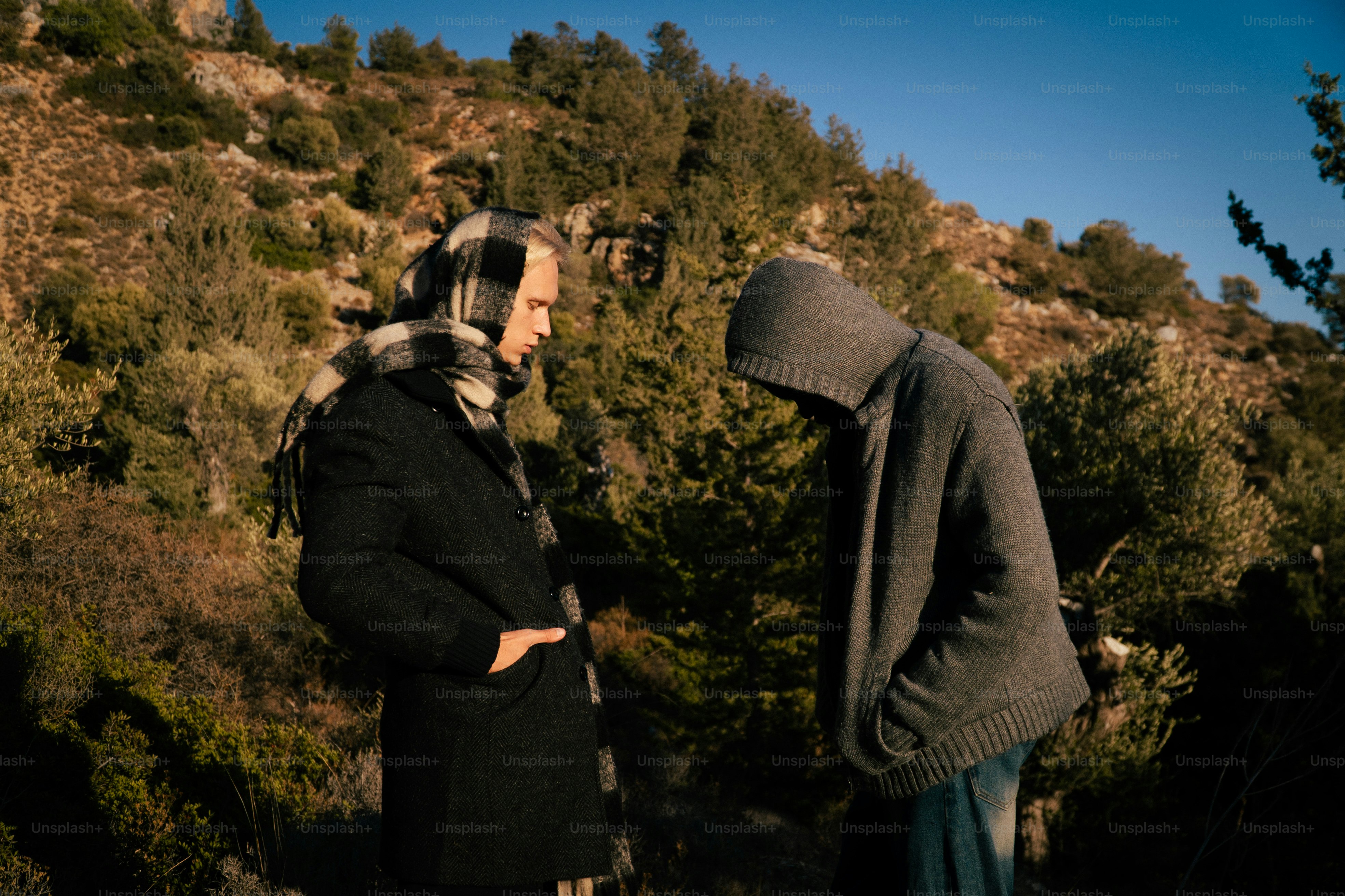 Two people stand in a wooded, rocky hillside.
