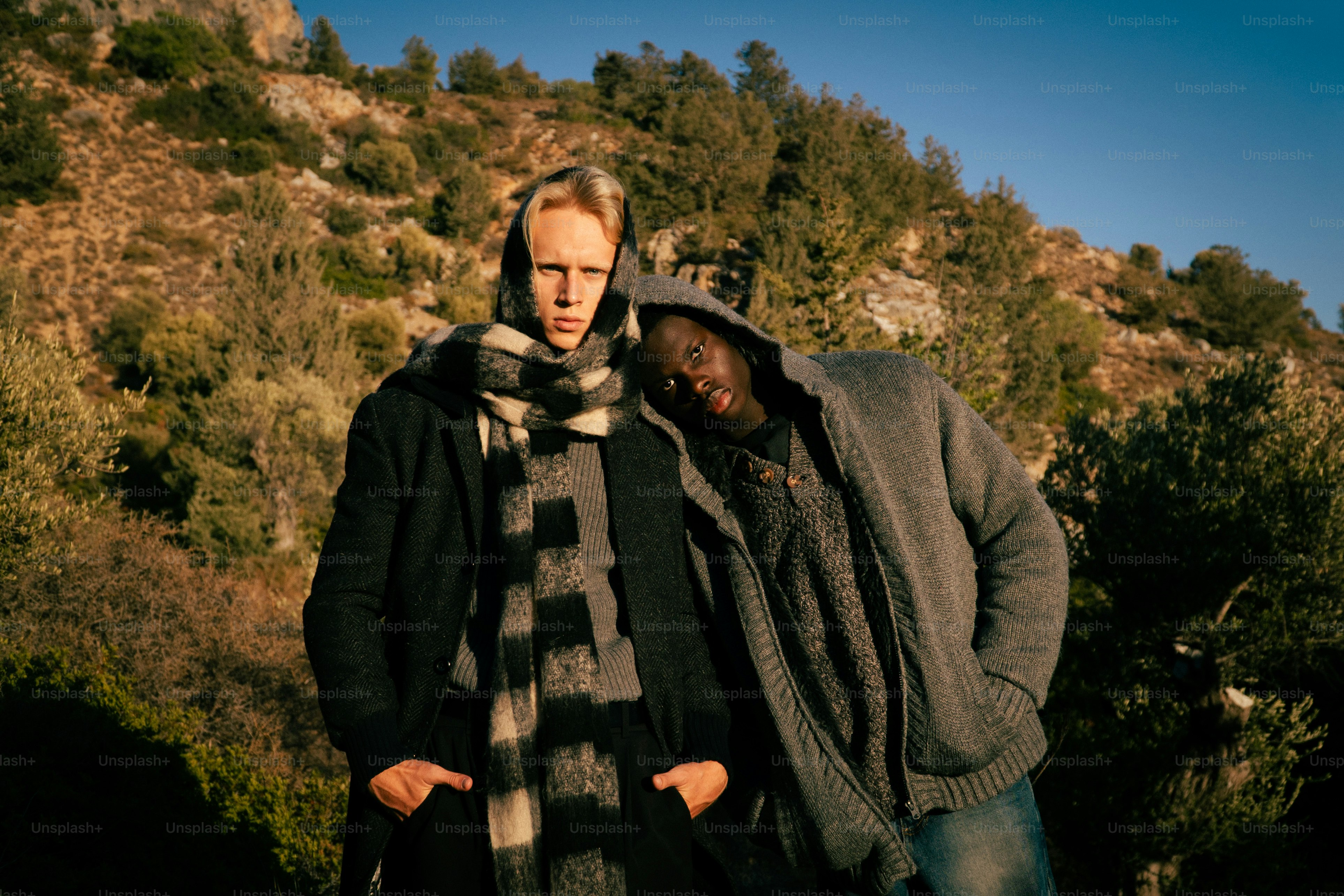 Two men standing outdoors with a wooded hillside behind them.