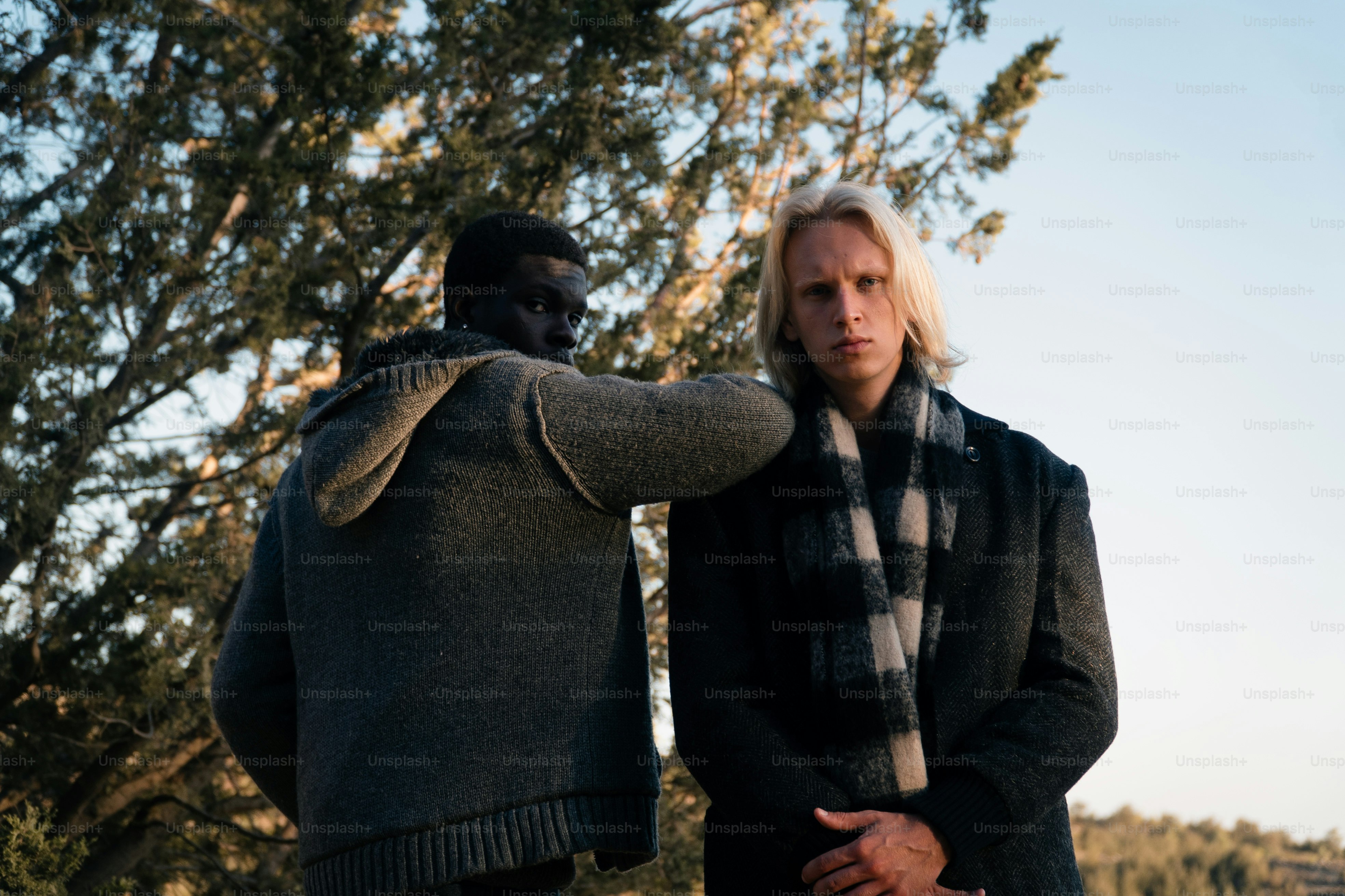 Two men standing outdoors with trees and sky