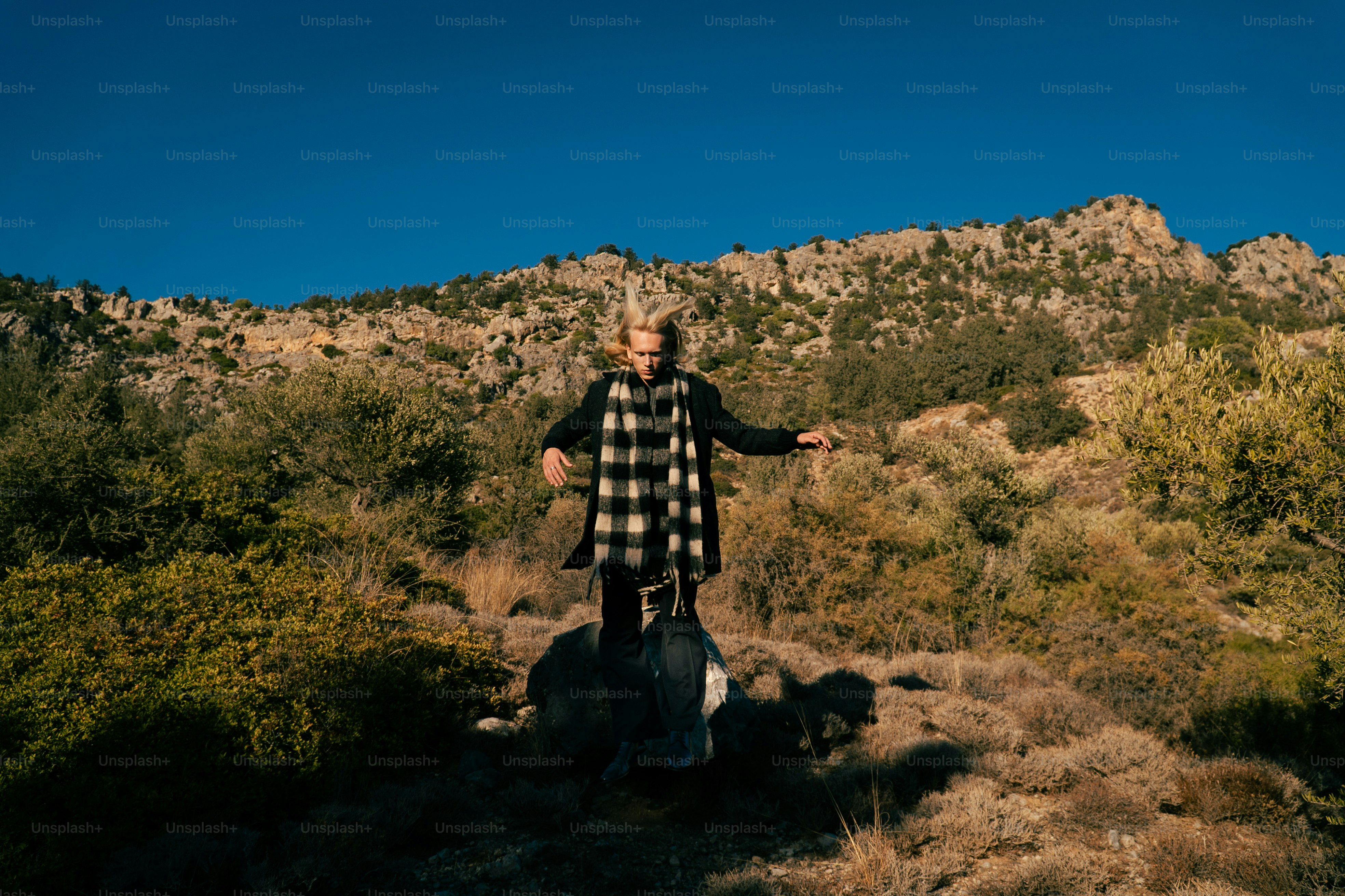 Woman standing on rocky hill with mountains behind her.