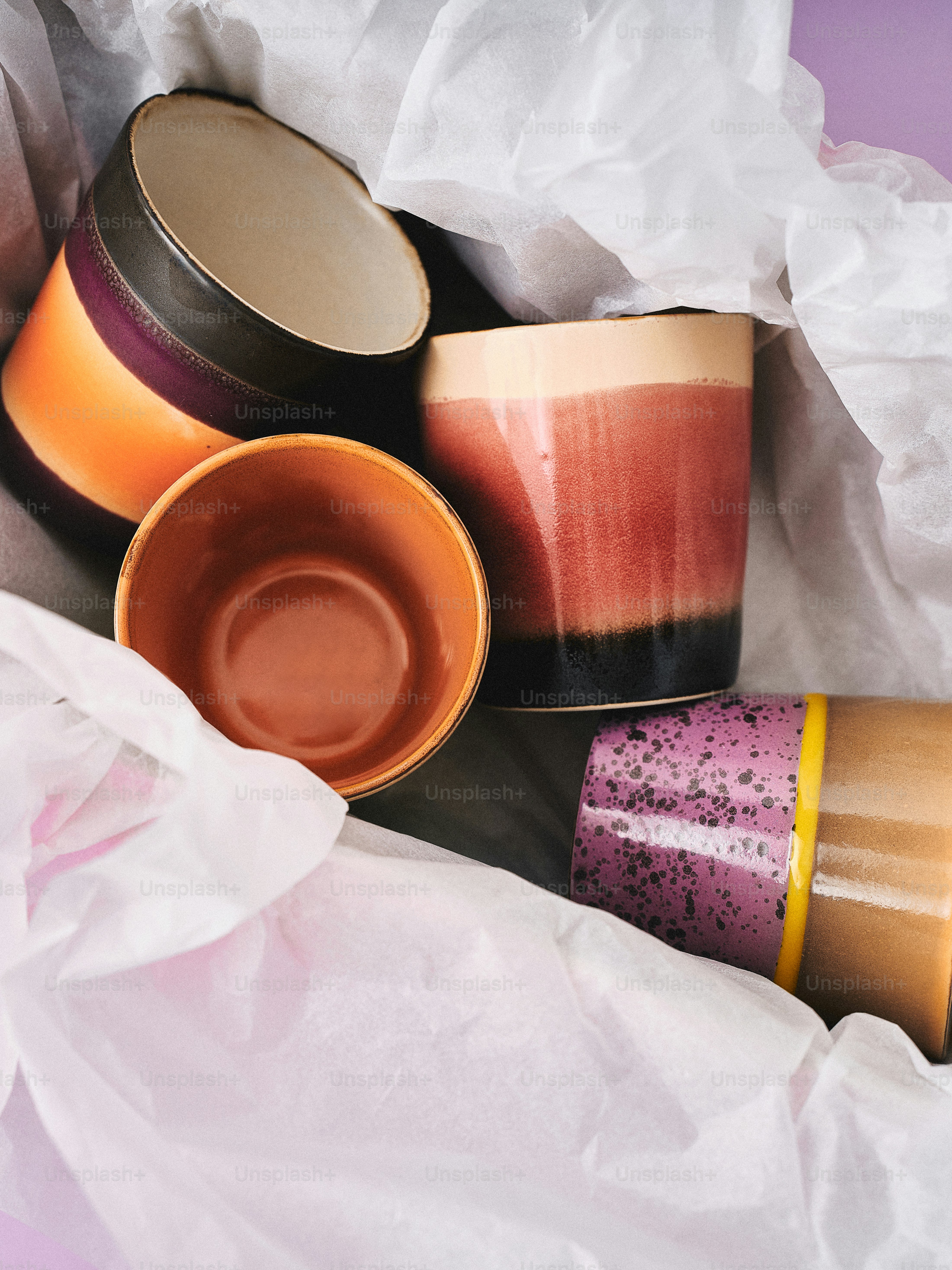 Quatre pots en céramique colorés enveloppés dans du papier de soie.