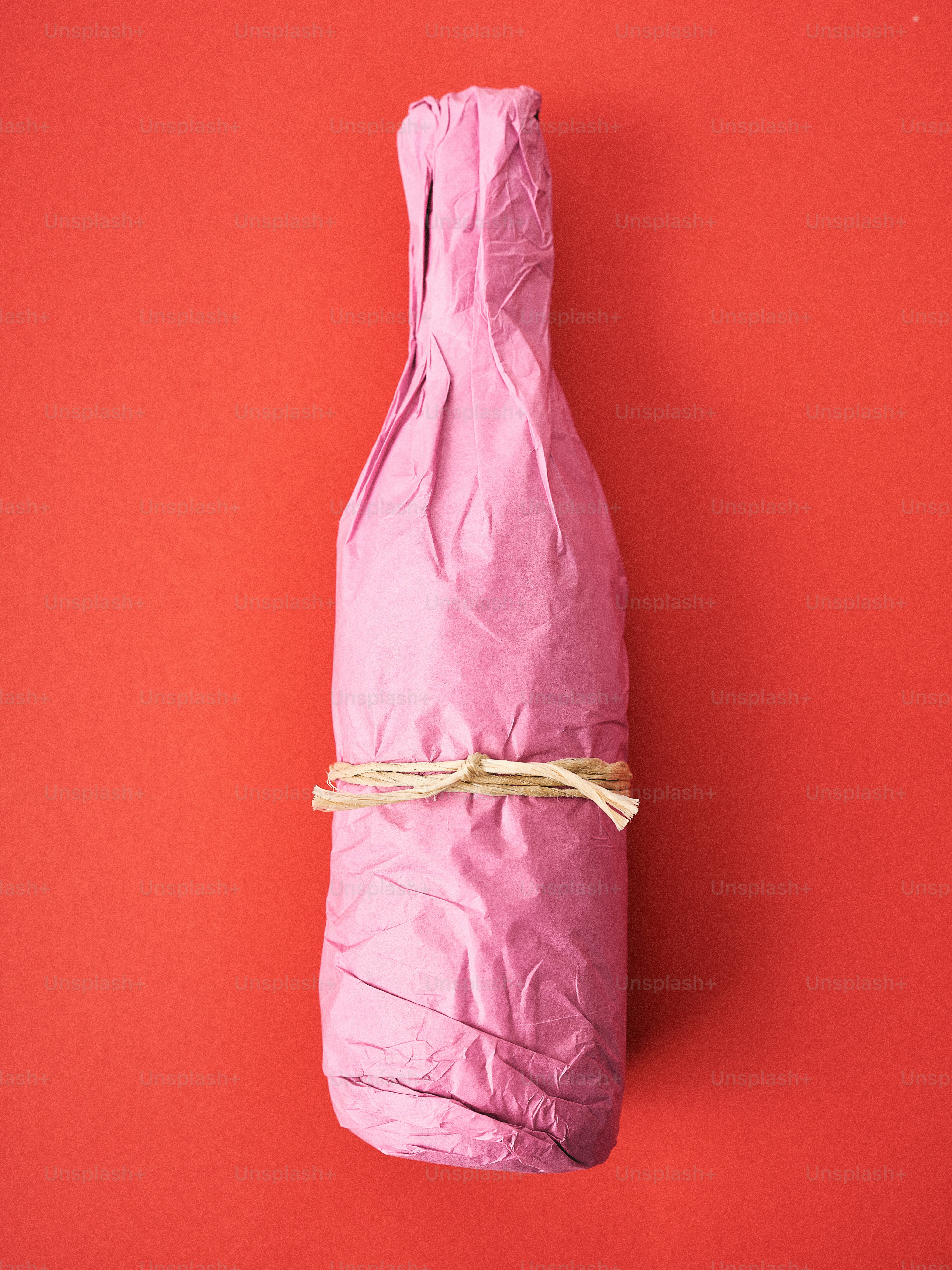 Pink wrapped bottle tied with twine on red background