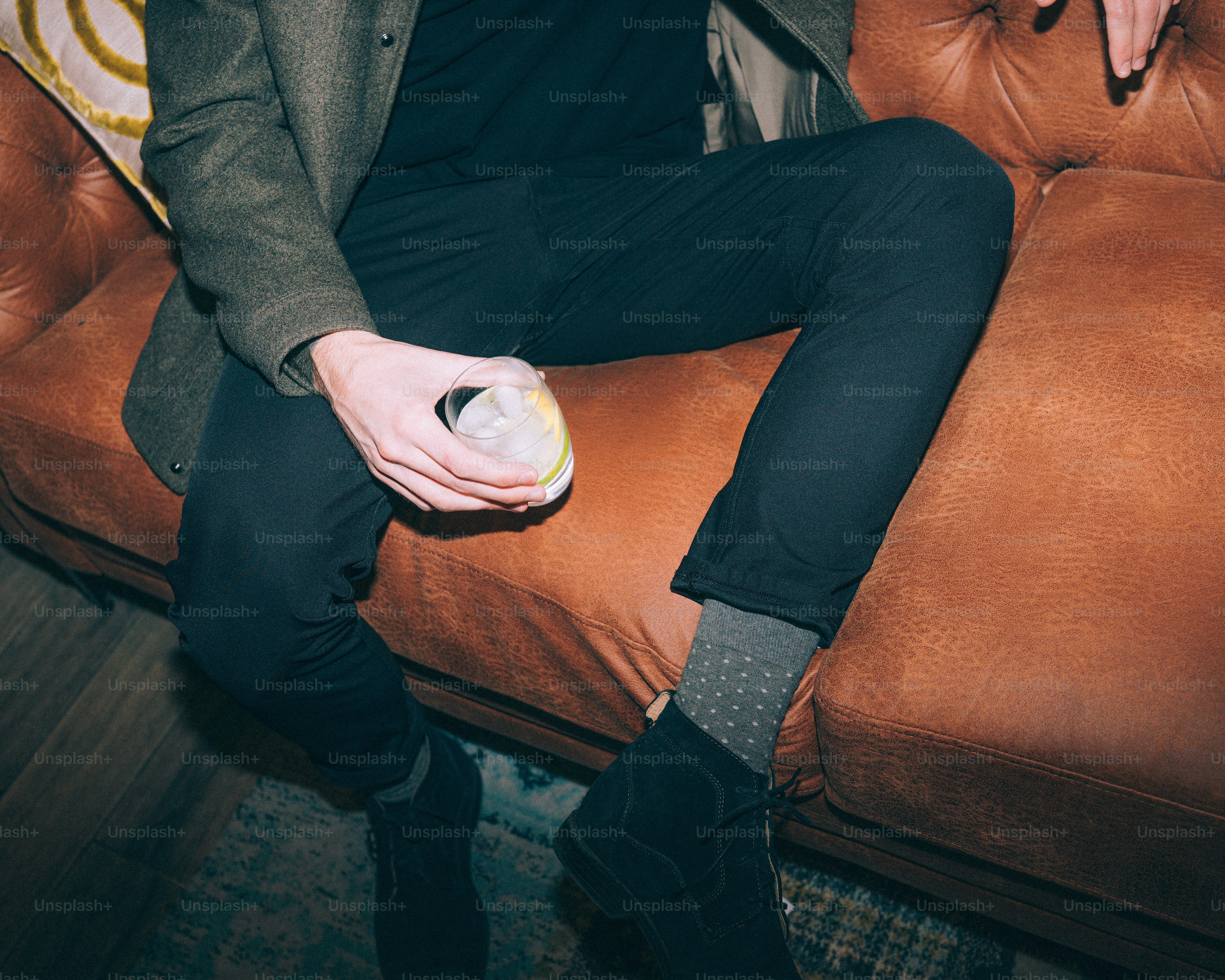 Man in dark clothes holding a glass on couch