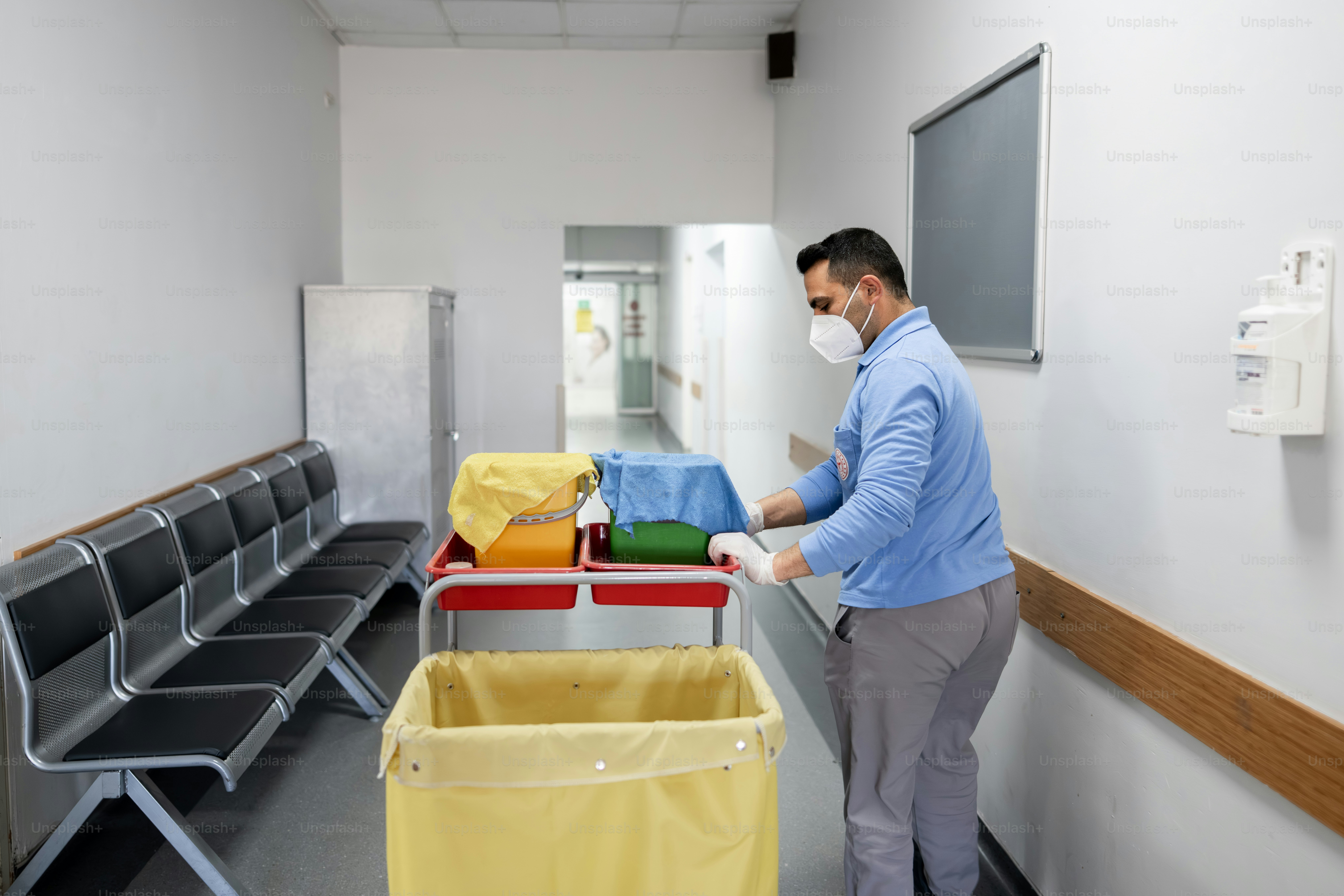 Man in mask pushes cleaning cart down hallway.