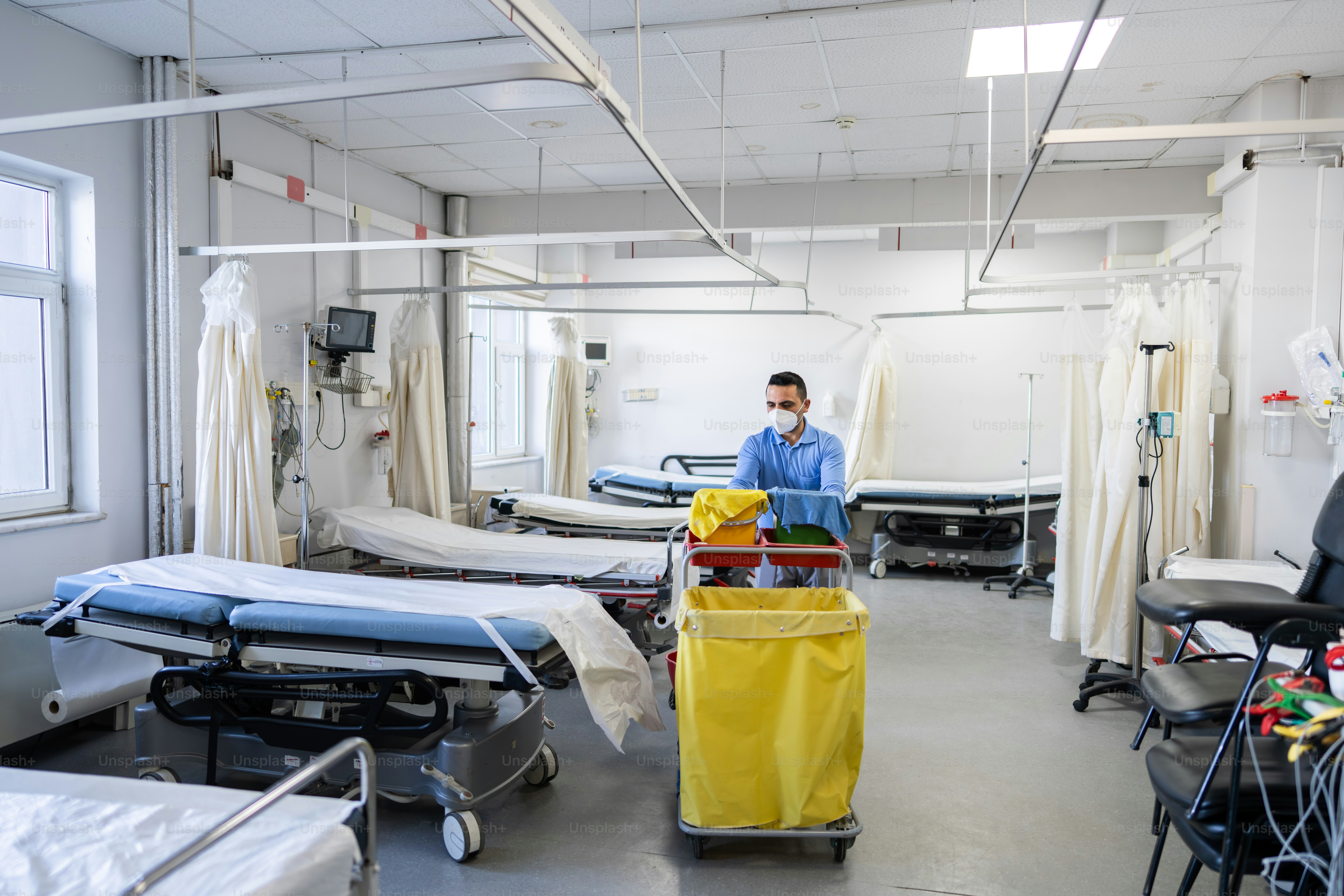 A cleaner pushes a cart through an empty hospital ward. photo ...